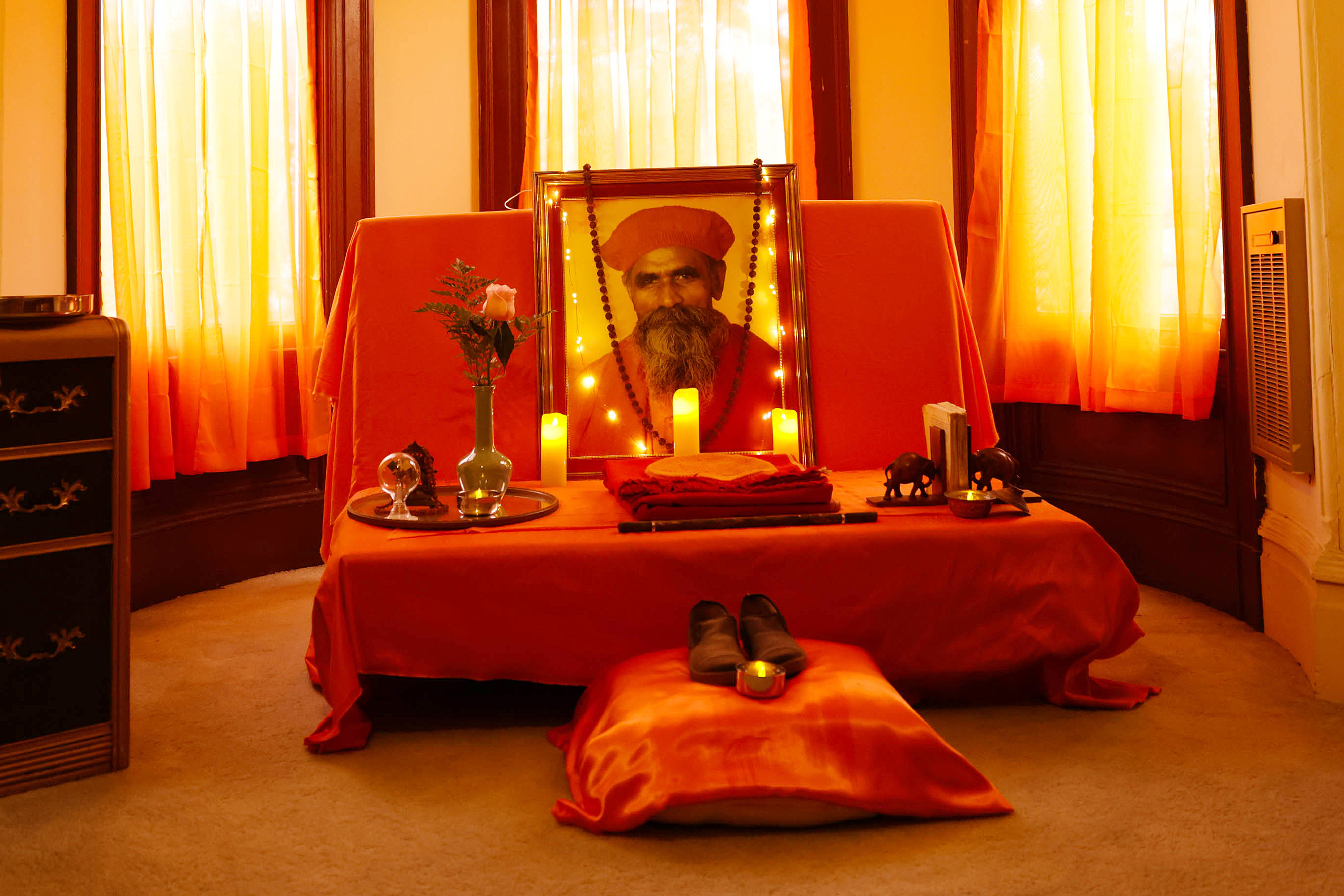 A shrine including candles, flowers and another items on a couch with the centerpiece photo of Shri Brahmananda Sarasvati.
