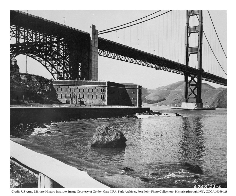 A black and white image partially showing the Golden Gate Bridge and the Fort Point Historic Site, as well as wooden post and rail barriers from 1947.