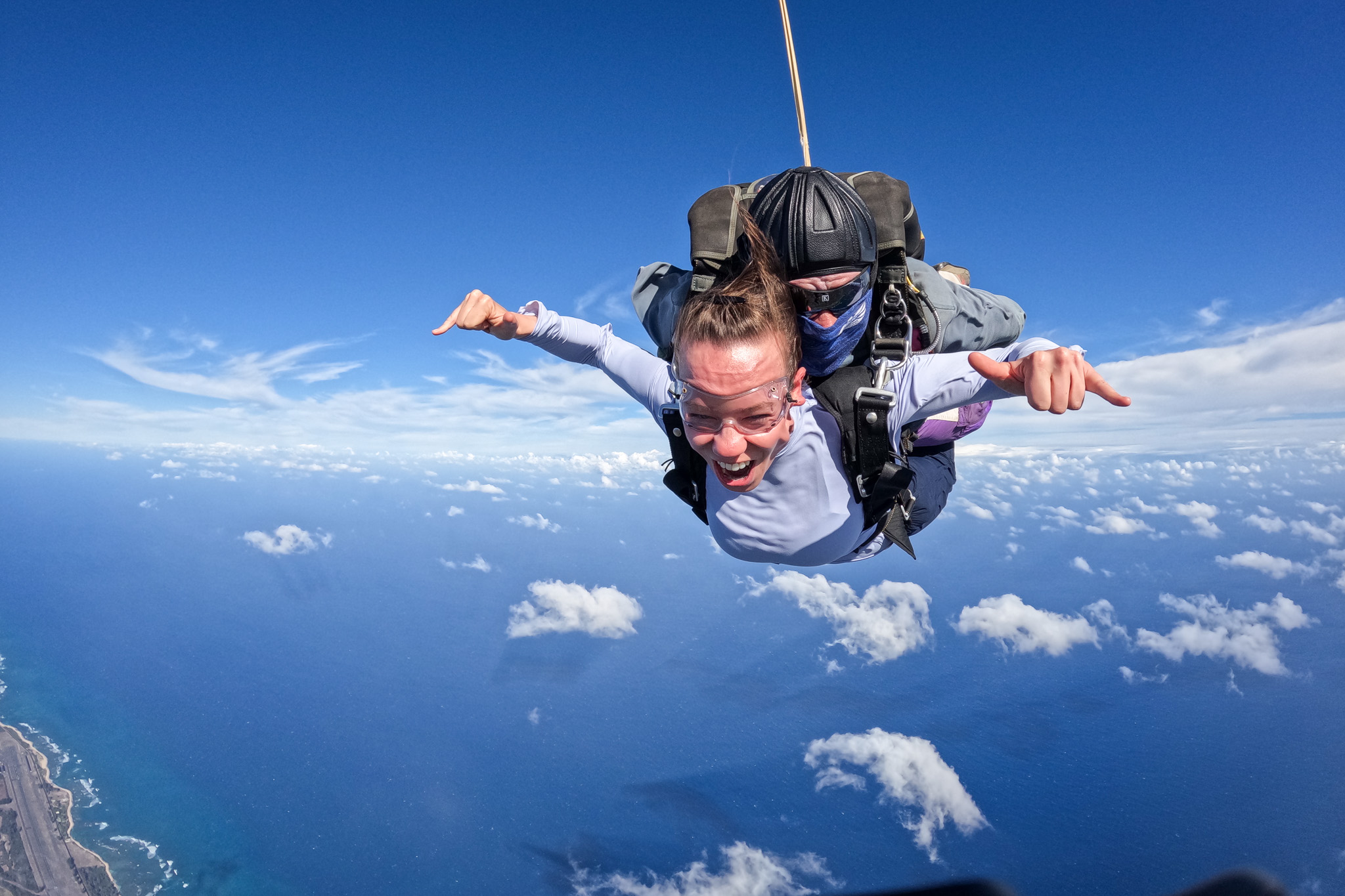 A woman smiles mid-air skydiving, surrounded by blue sky.