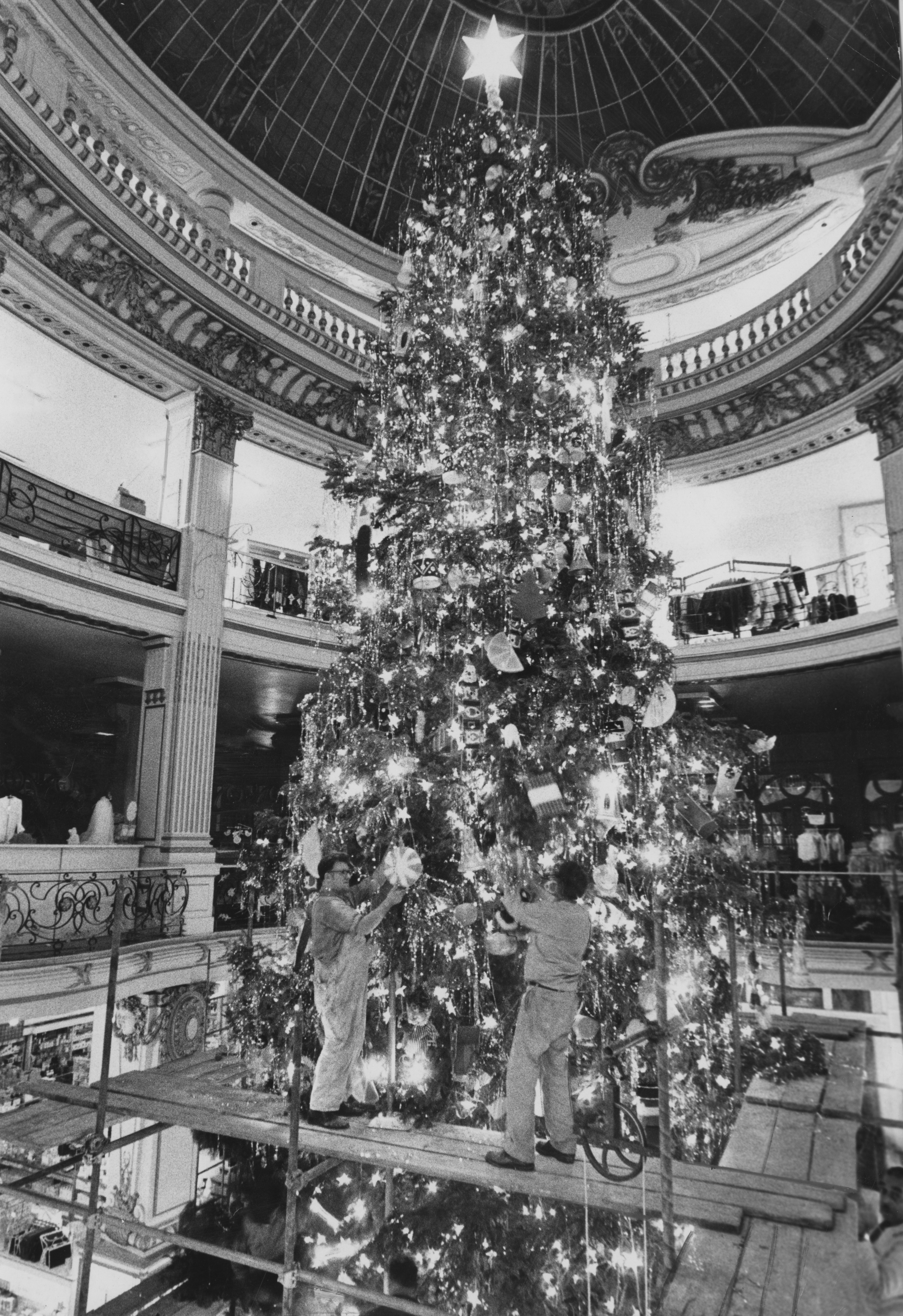 Two workers in front of a tall Christmas tree.