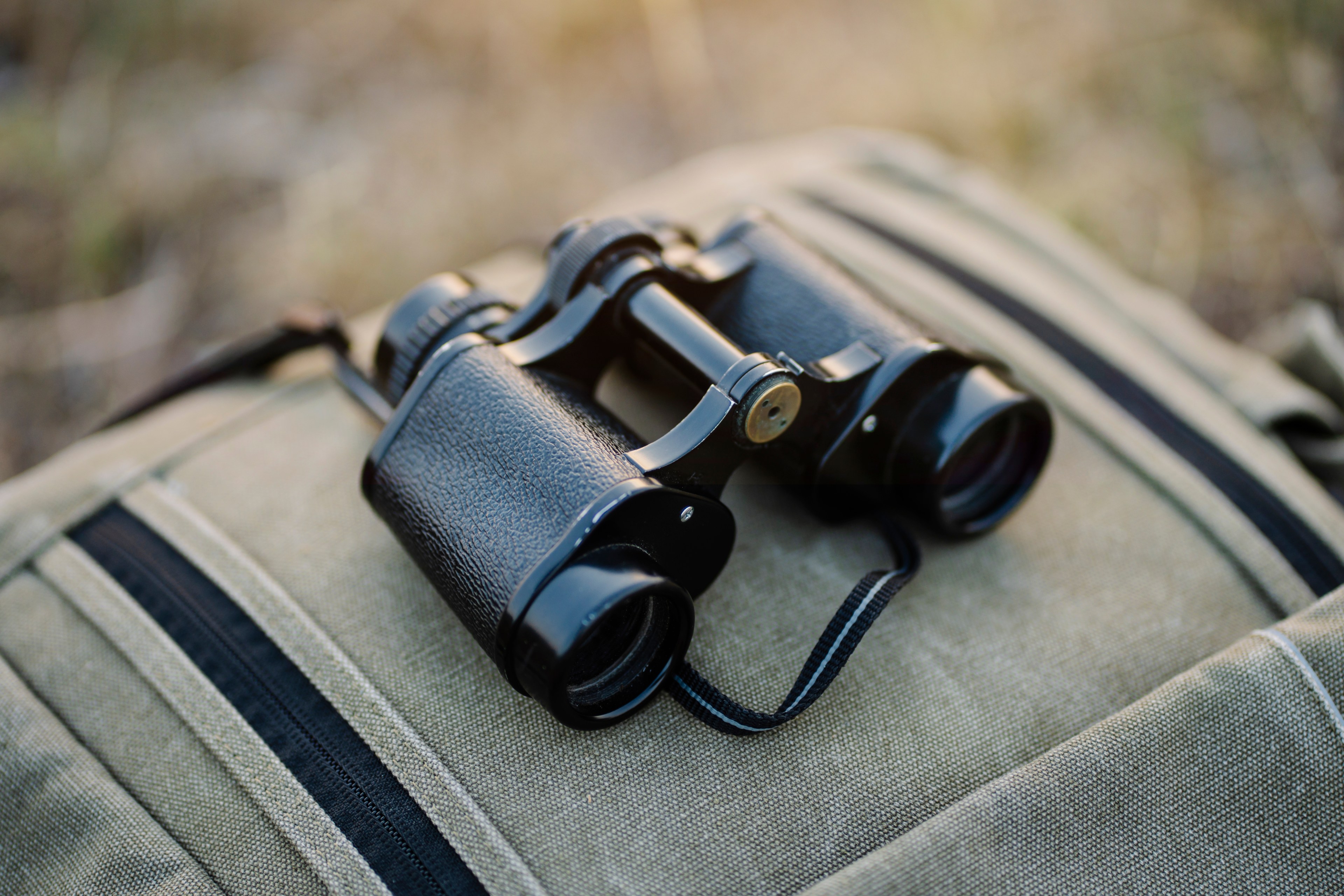 A pair of old binoculars rests on a striped canvas bag in a natural outdoor setting.