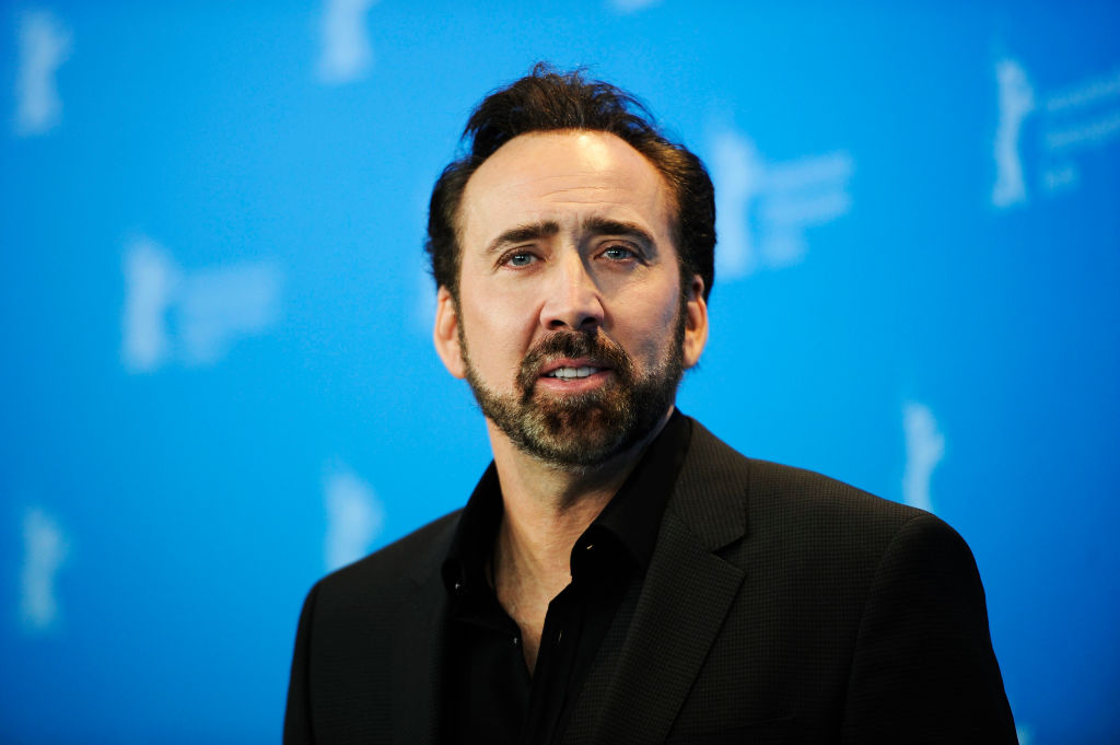 A man in a black dress shirt poses for cameras in front of a blue background.