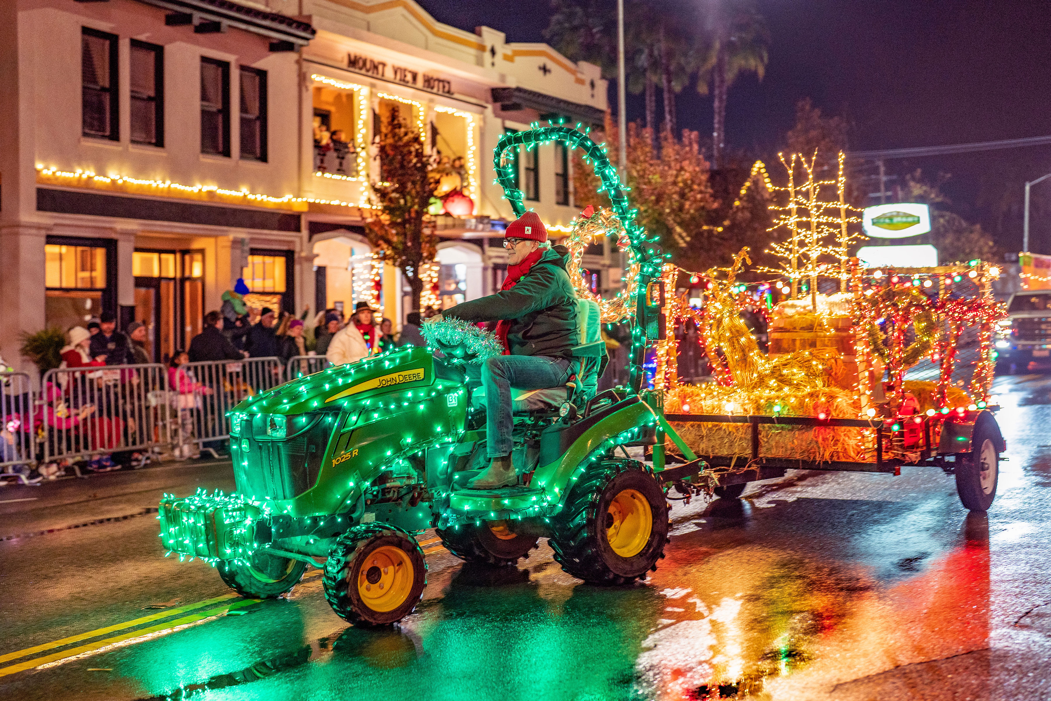 A man drives a green John Deere tractor illuminated in green holiday lights.