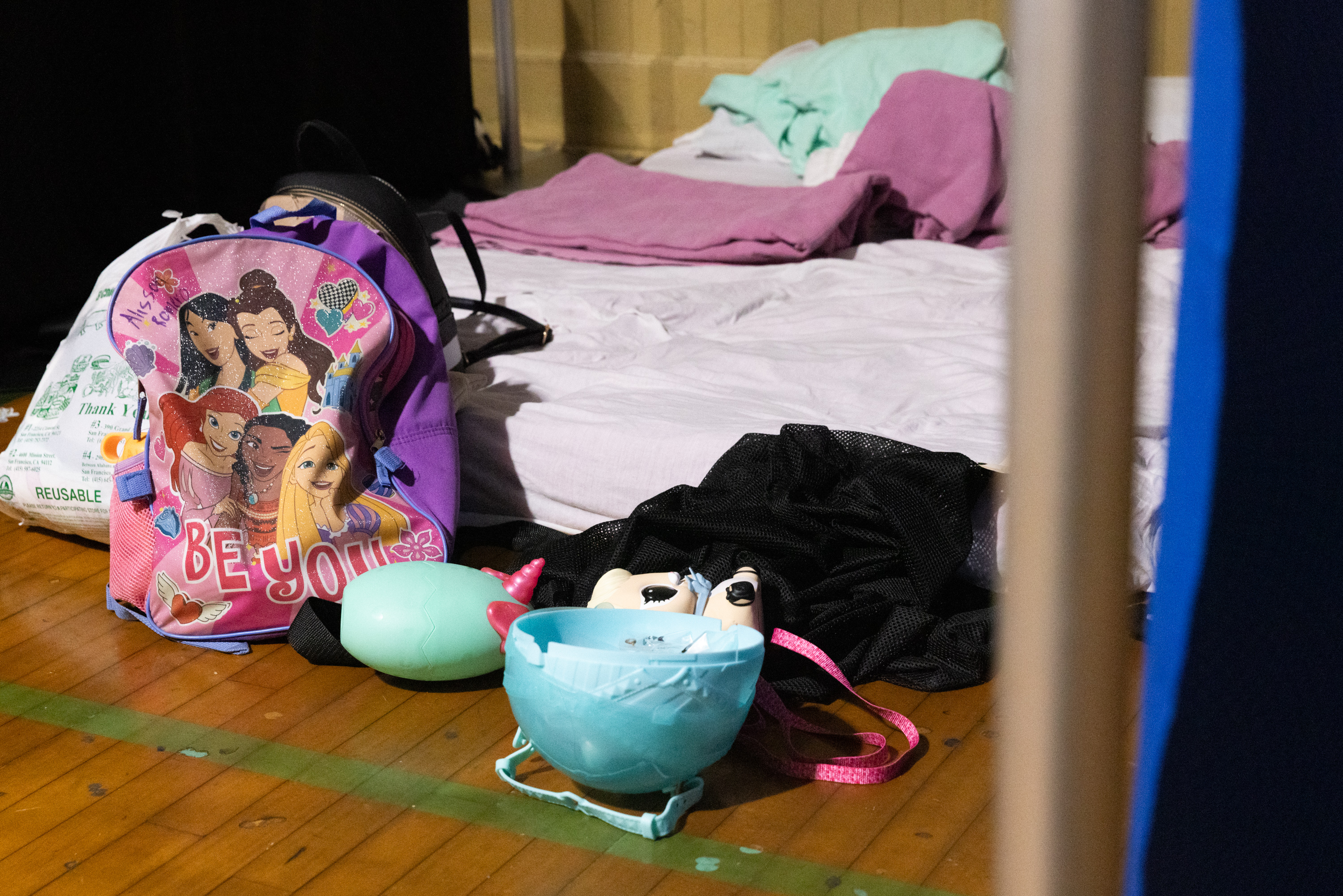 A Disney princess backpack beside a. mattress on a floor.