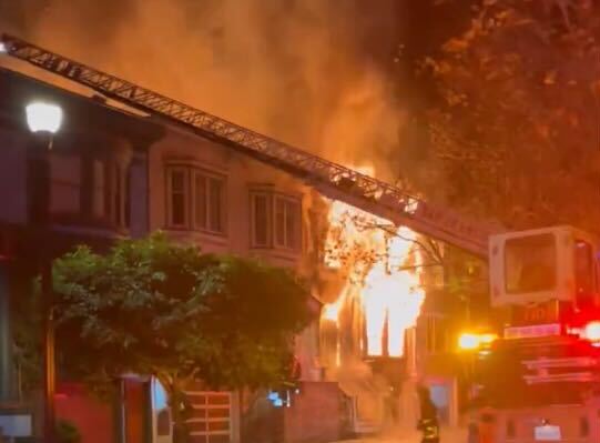 Flames shoot from the front of a three-floor duplex apartment building.