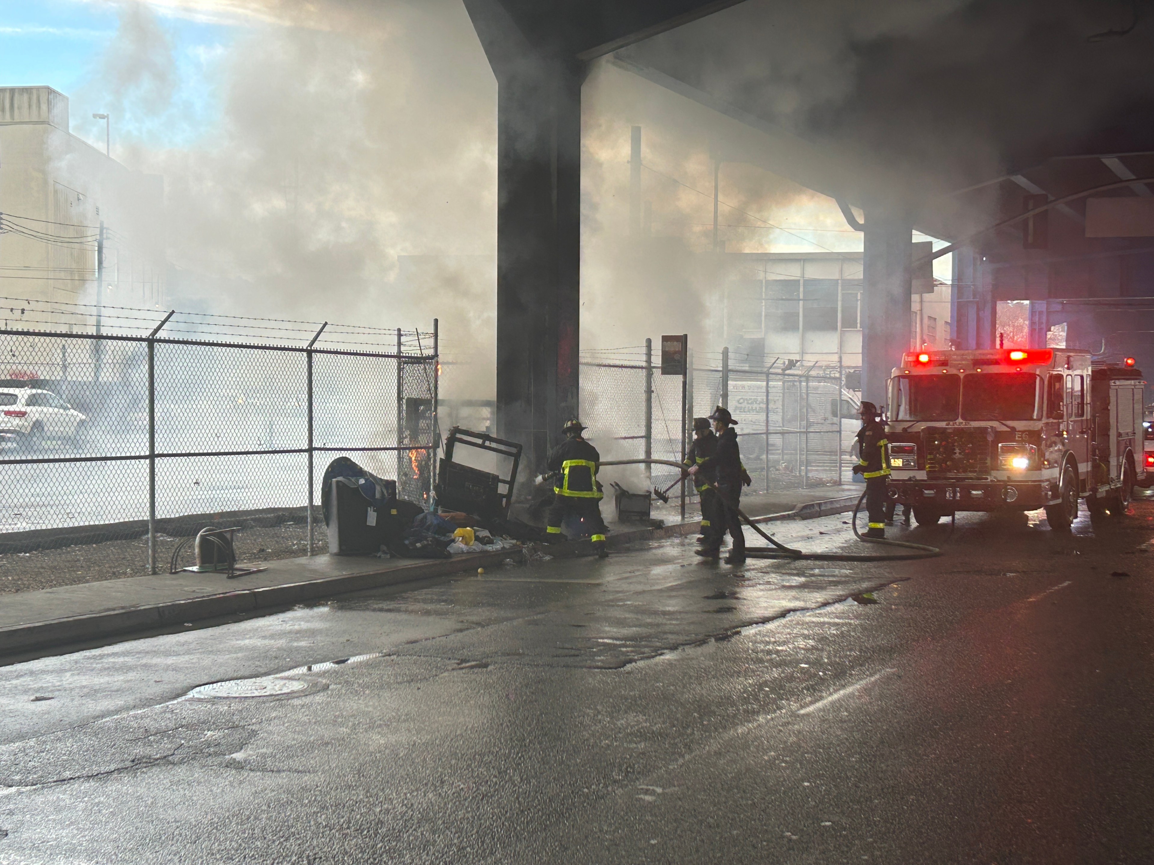 Firefighters spray water on a fire at the base of an elevated freeway support pillar.