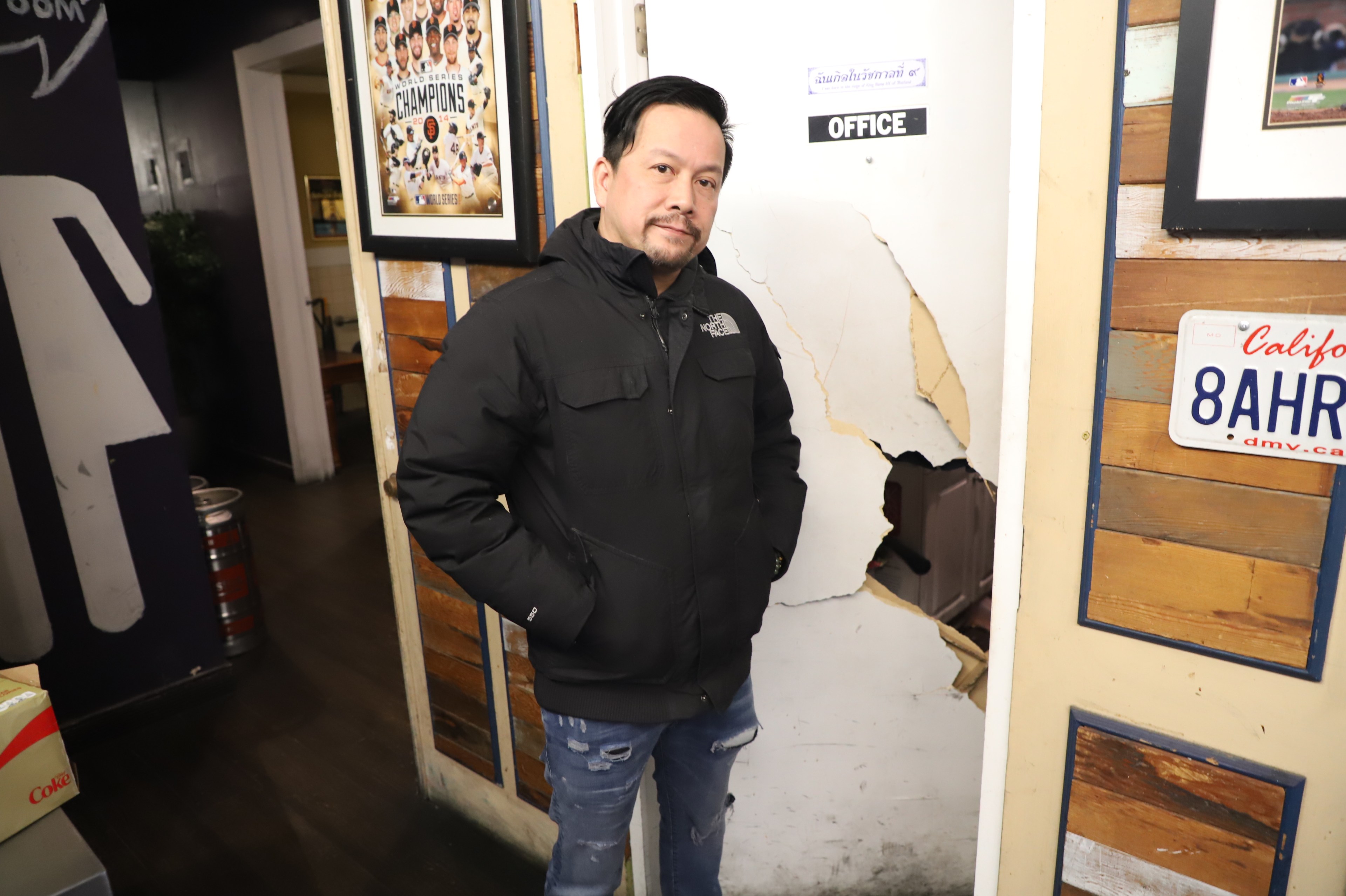A man stands in front of a broken-down door.