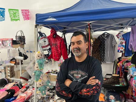 Man in black shirt stands in front of a stand with apparel