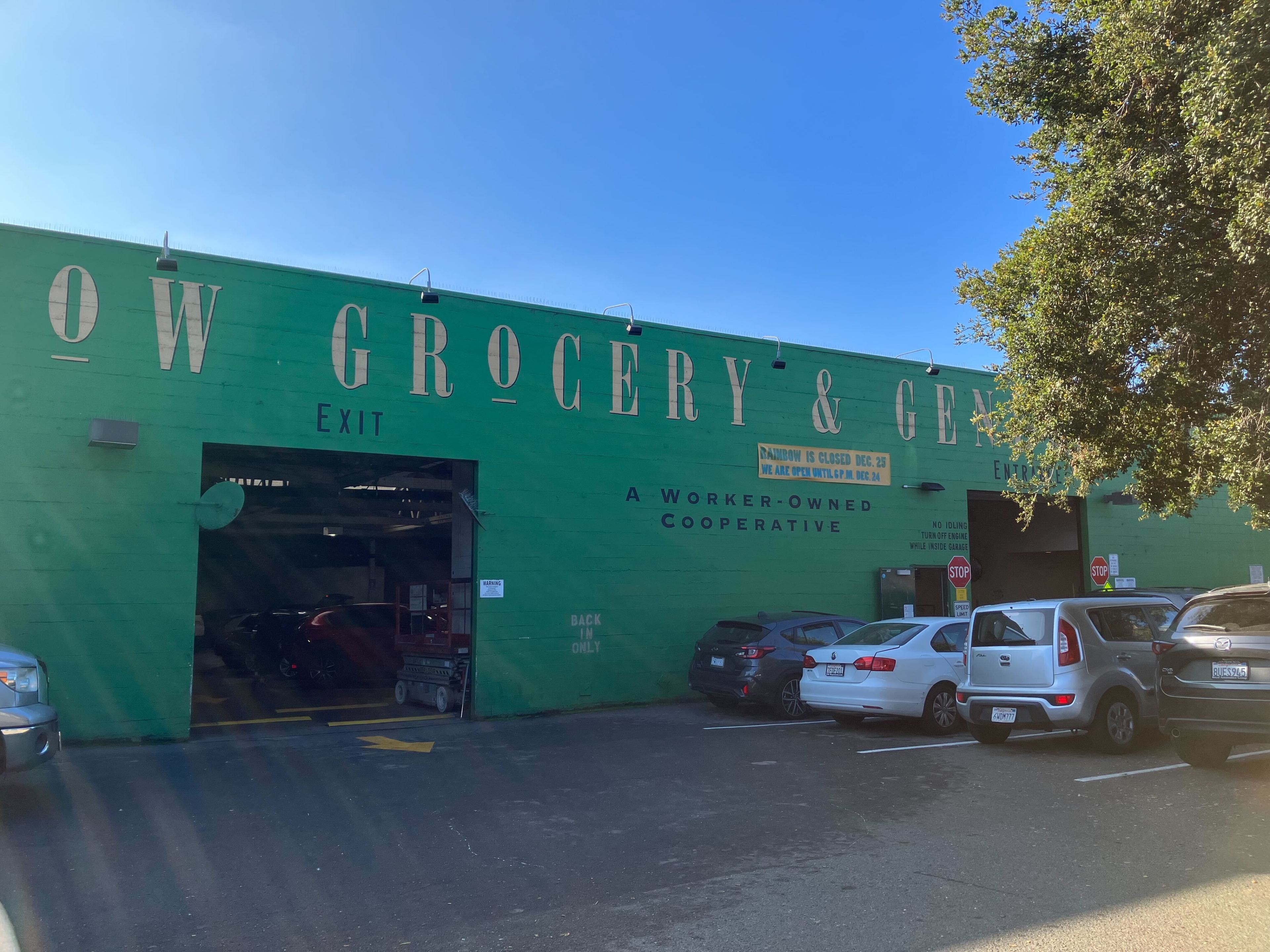 a warehouse is seen painted green with the word grocery above the entrance by parked cars