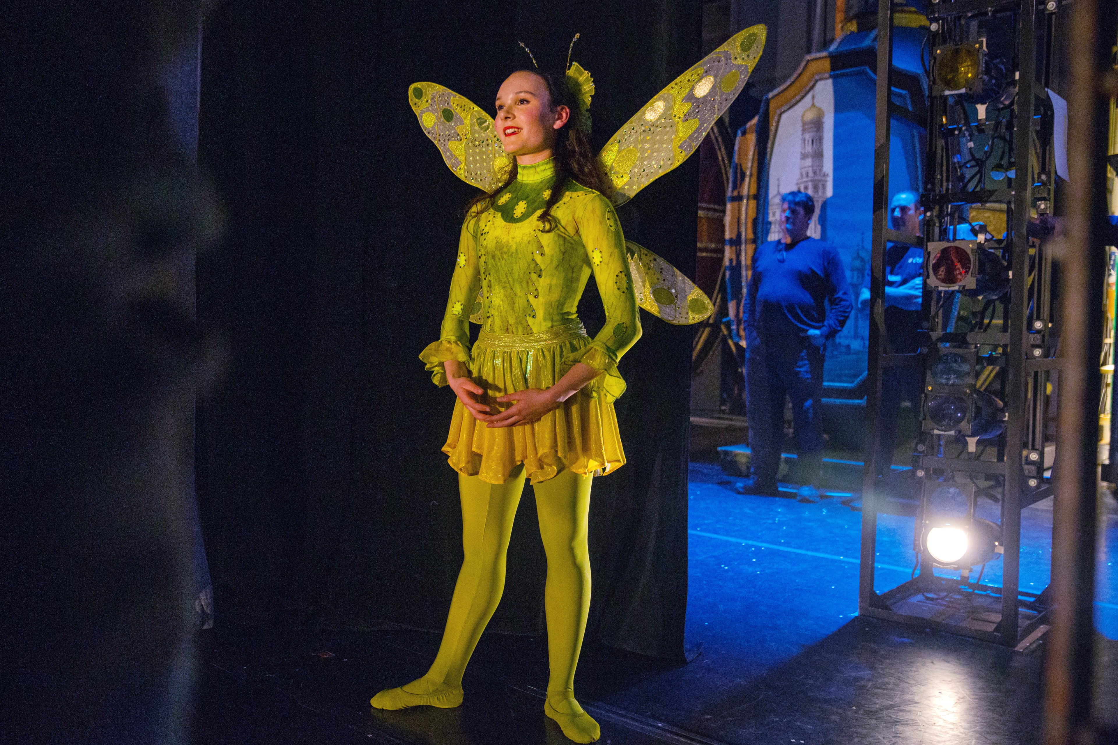 A woman dressed like a green butterfly waits backstage at a theatre