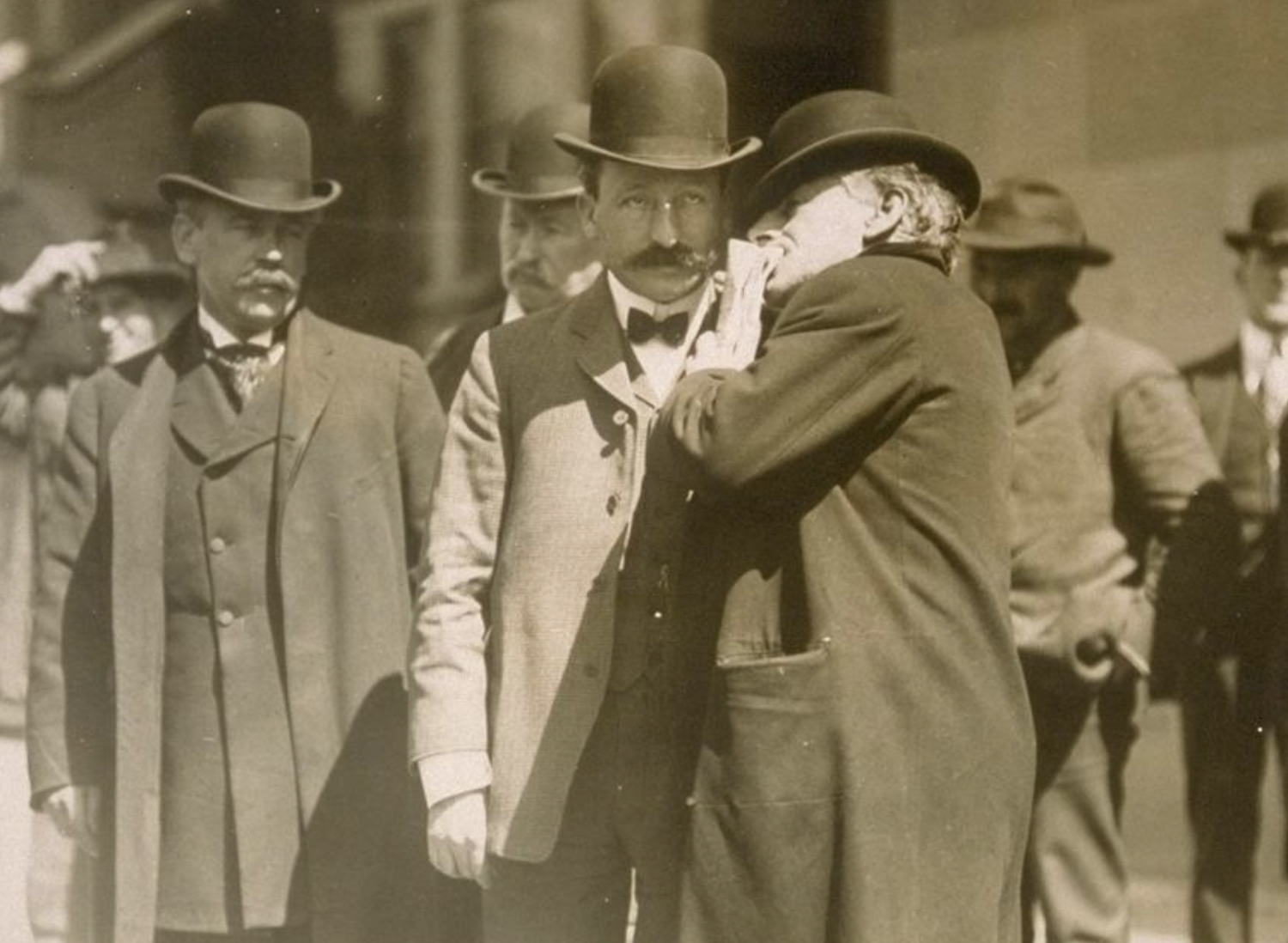 An archival photo of a man whispering in the ear of another man sometime in the early 1900s.