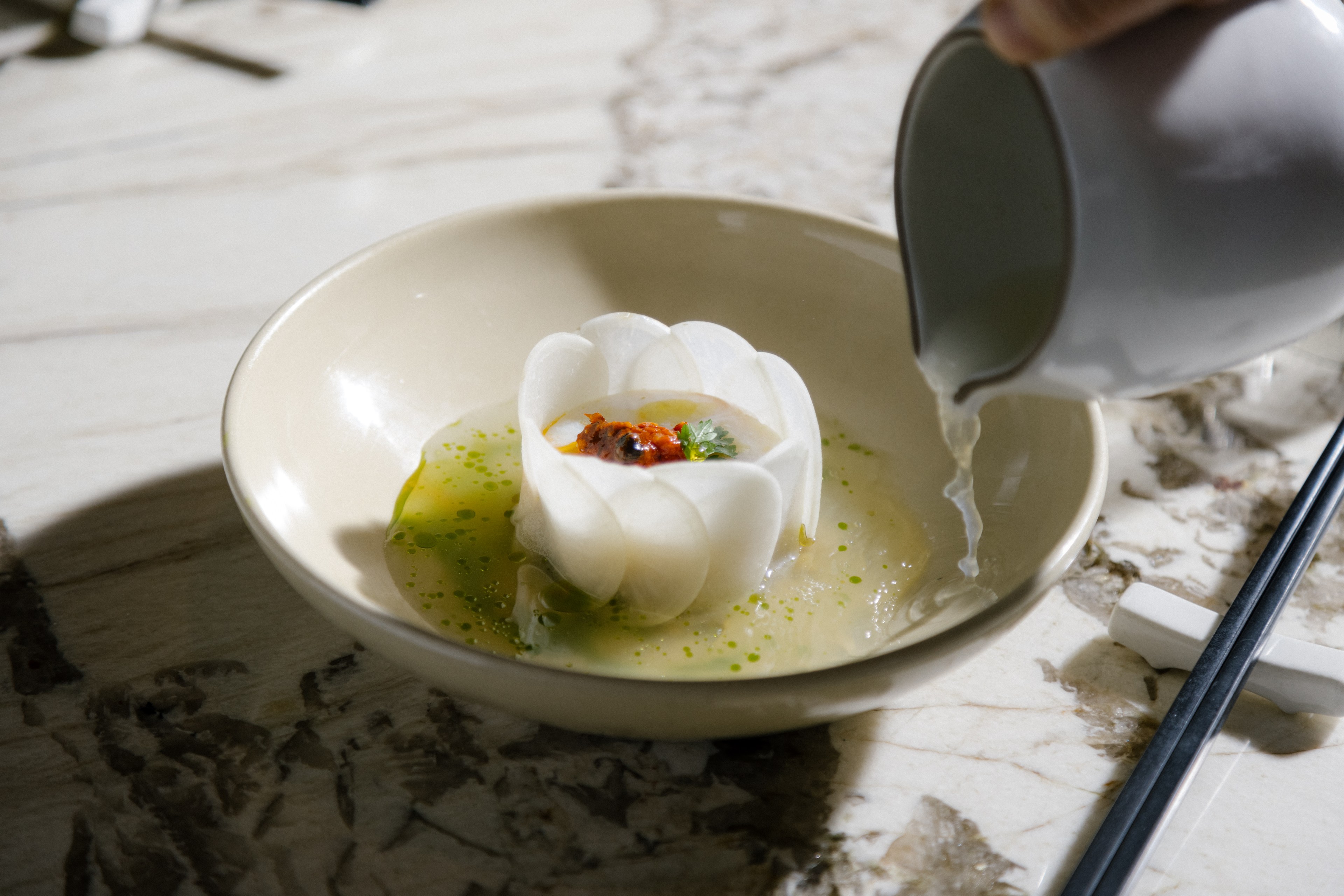 Chef Brandon Jew plating suan cai yu: ling cod, kohlrabi, pepperoncini, and clam broth