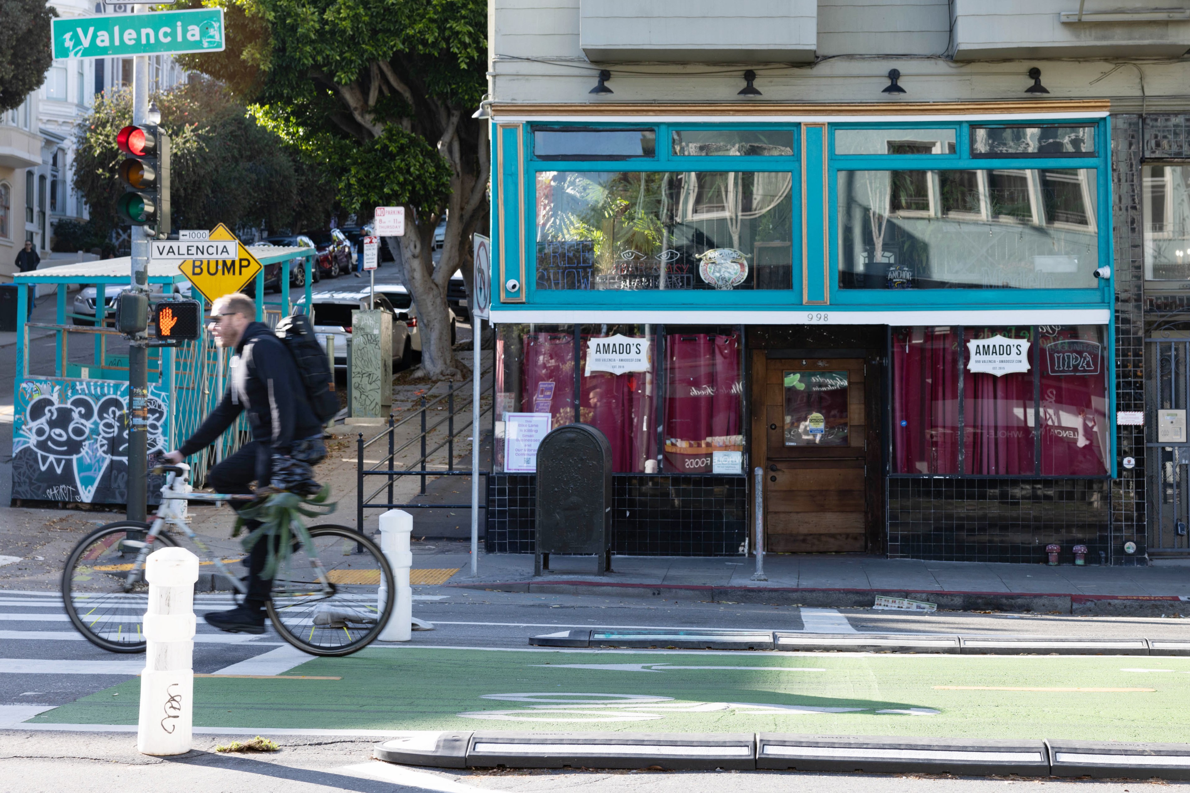 A cyclist passes by a shuttered nightclub facade on a street in daytime.