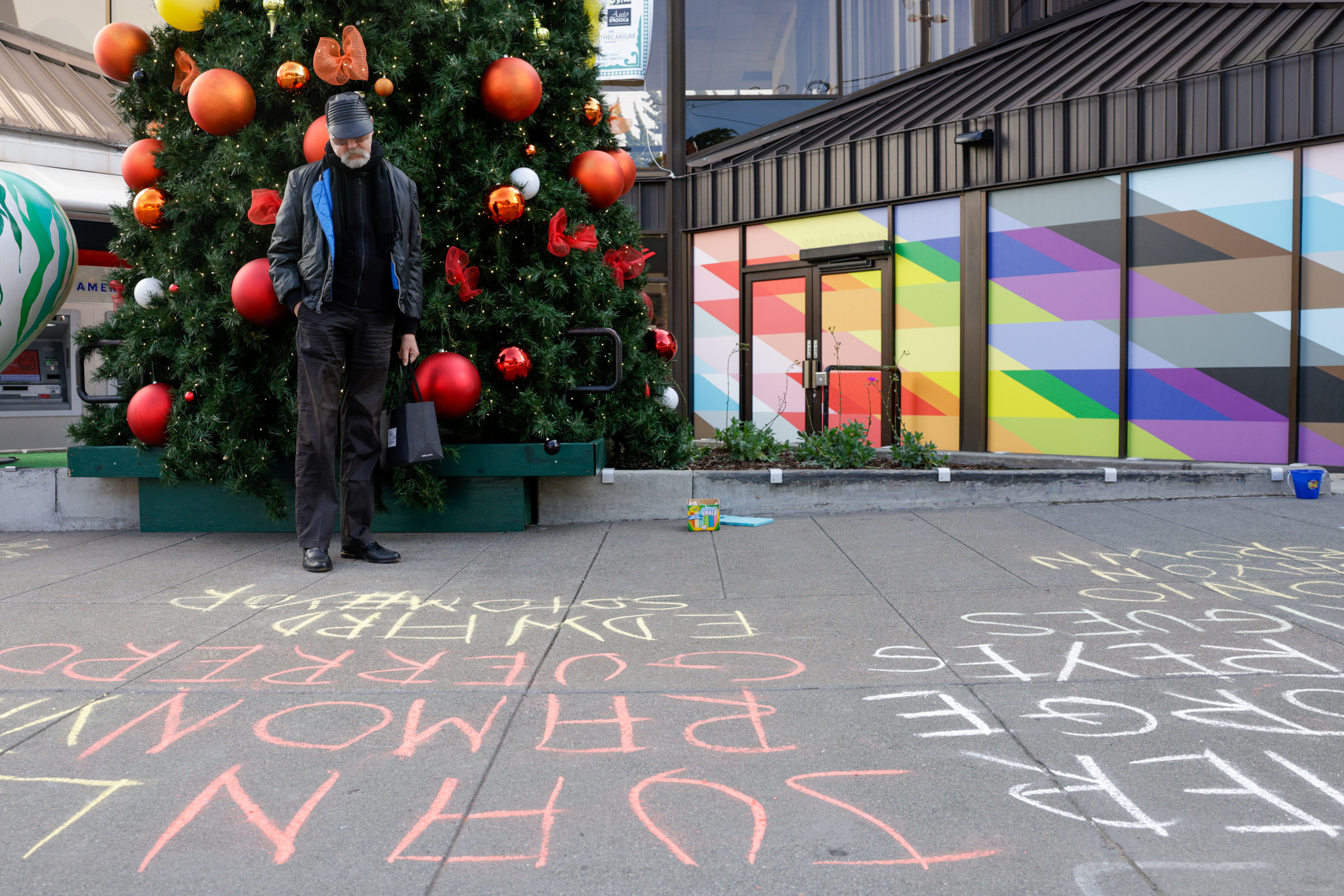A person in a black hat reads the names of people on the sidewalk written in chalk during World AIDS Day.