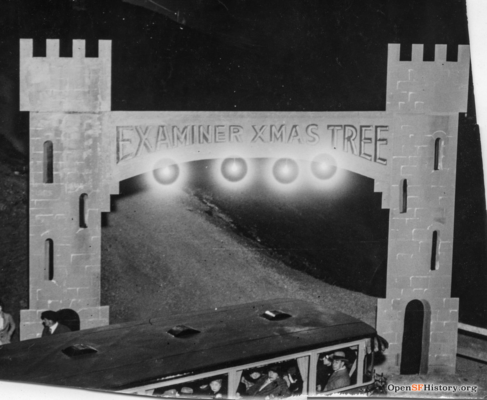 A medieval-style castle gate welcomes tourists in a black and white image taken at night.
