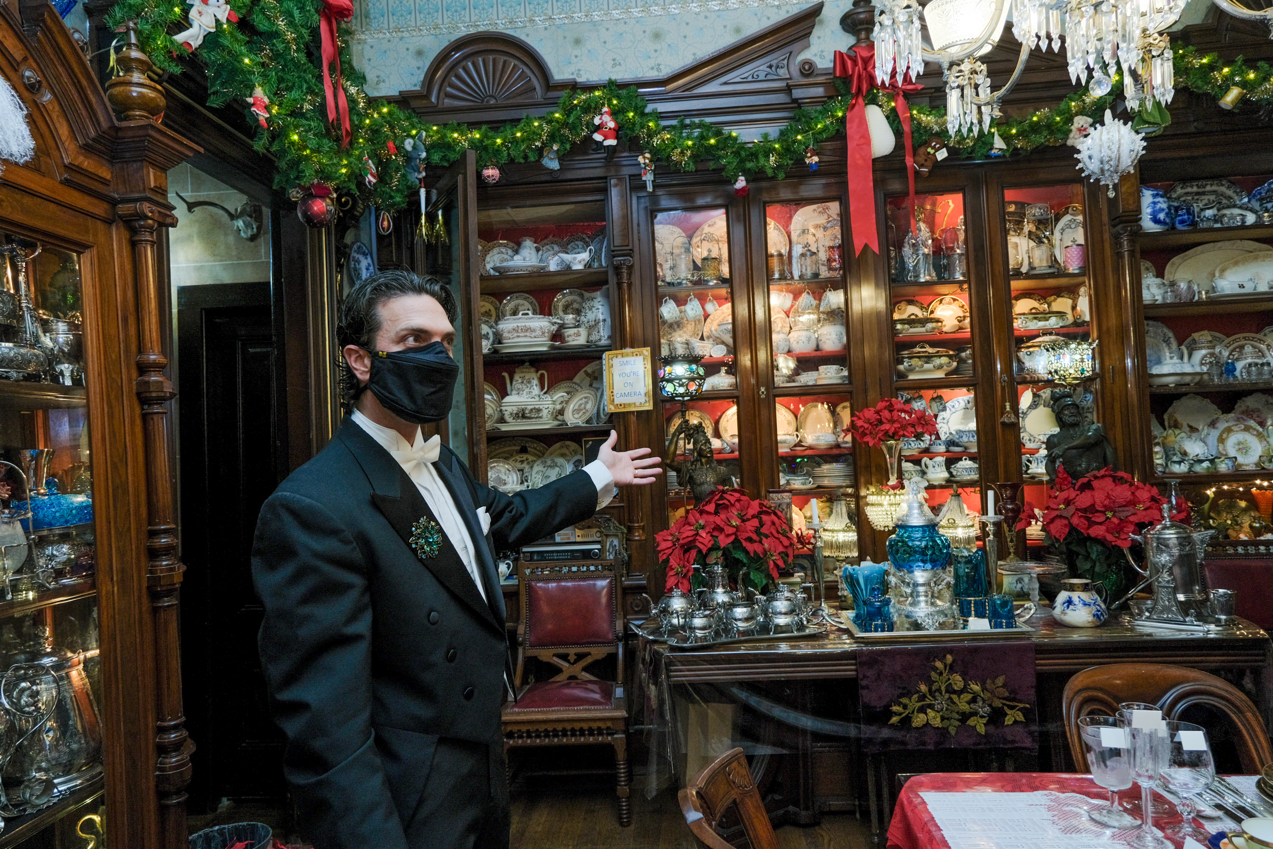 A person in a black suit jacket shows parts of the old victorian house that is decorated in Christmas decor.