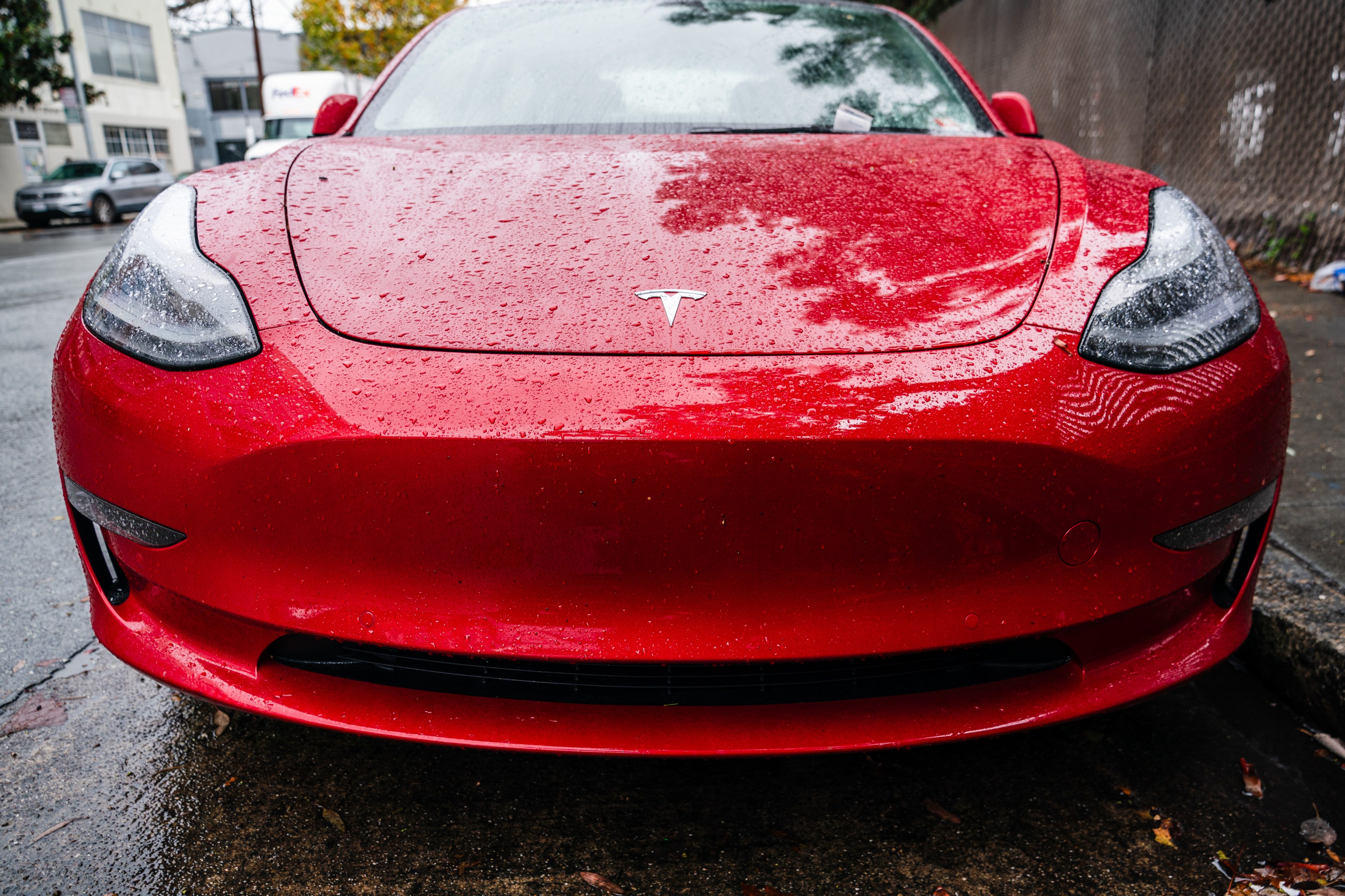 A red Tesla Model 3 with no front license plate.