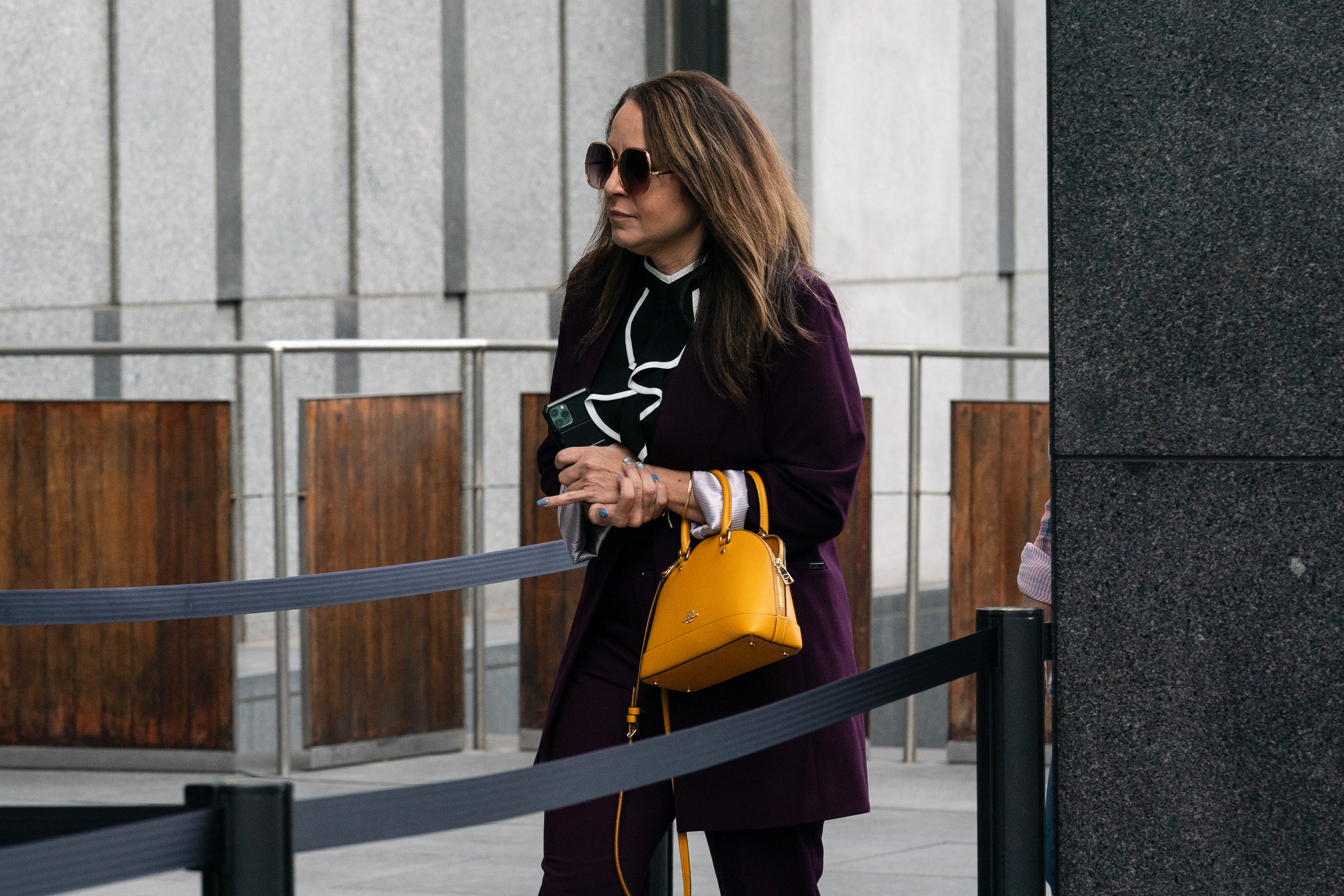 A woman with dark glasses and a yellow handbag walks between a sectioned off area on the sidewalk
