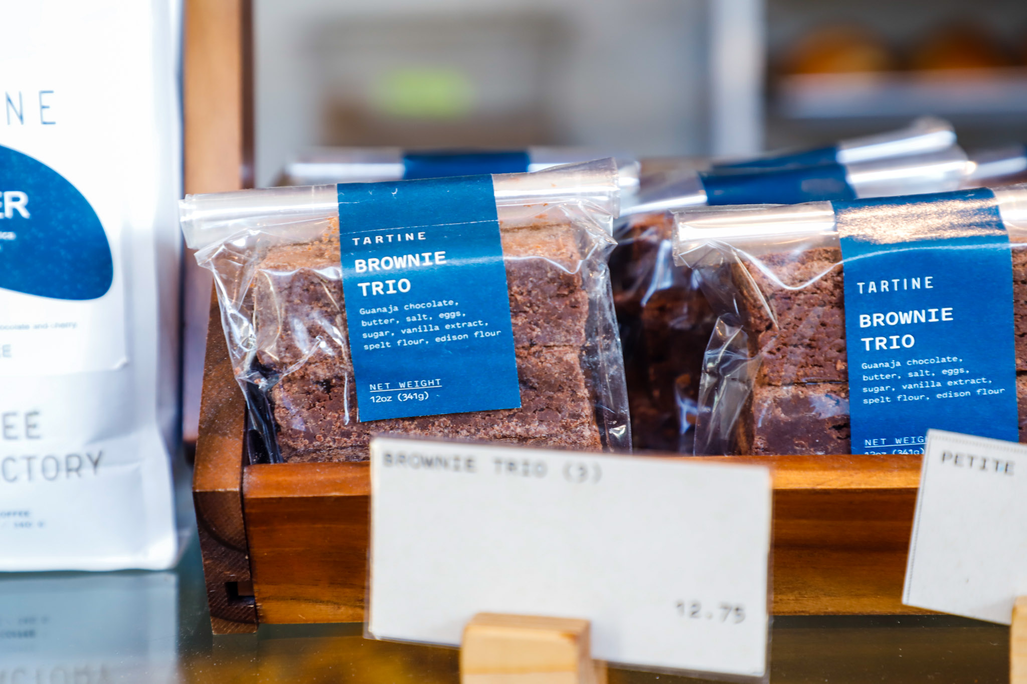 Two packages of brownies sit side by side on display at a bakery with the label &quot;tartine brownie trio&quot; on them in blue.