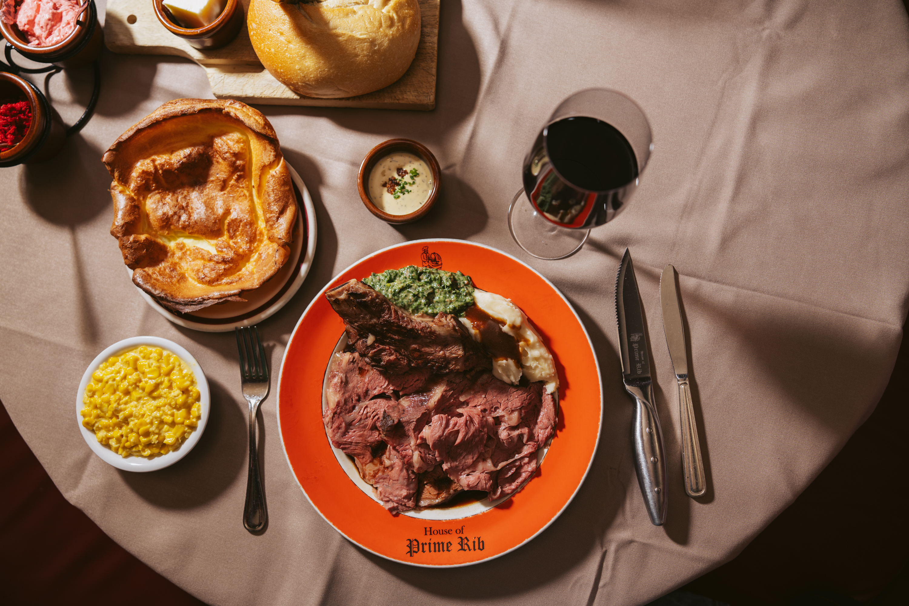 A prime rib on a plate next to a fork, wine glass, and other items of food.