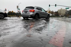 Cars drive through moderate flooding in an intersection.