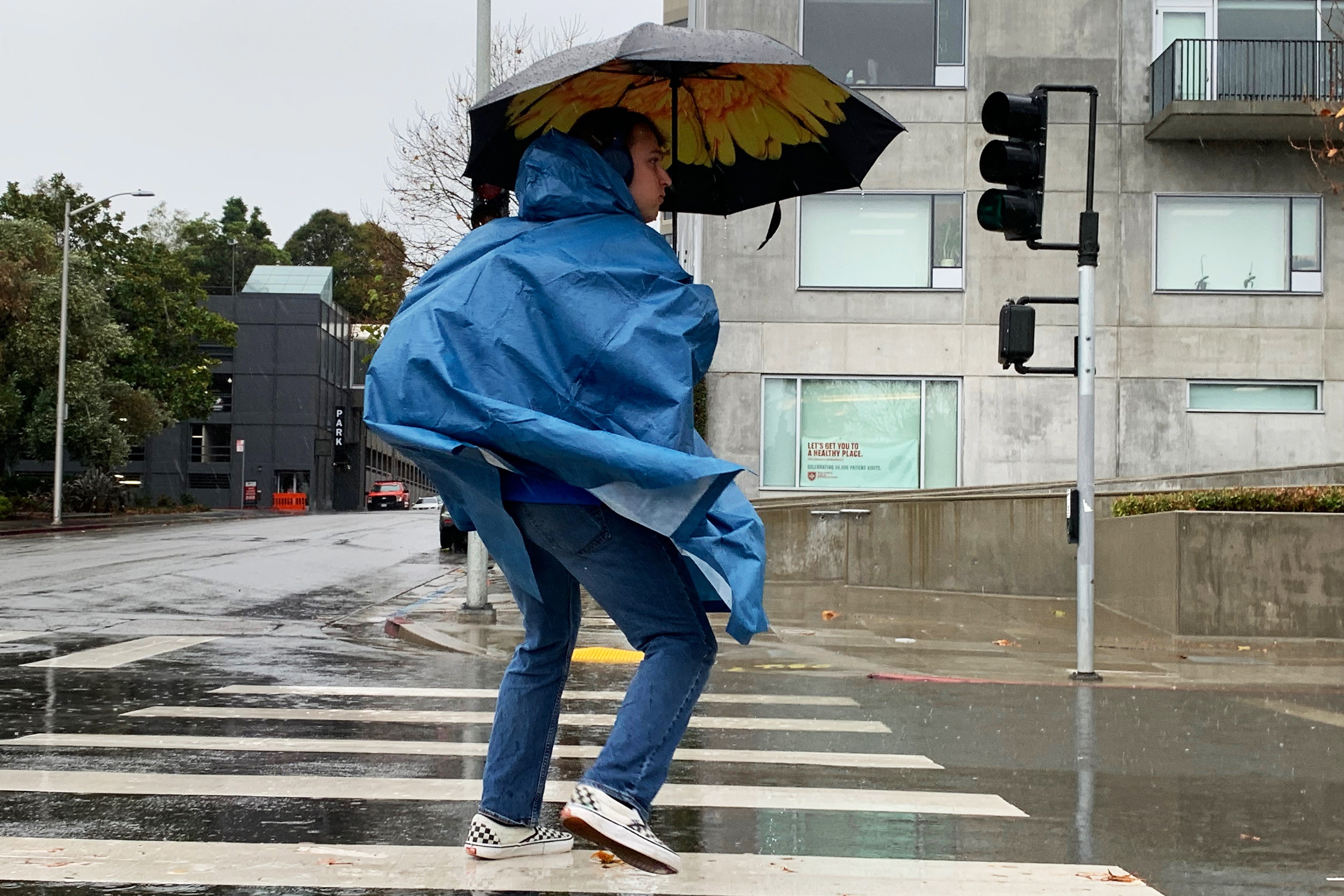 A person holding an umbrella waits for oncoming cars to pass before walking through a crosswalk.