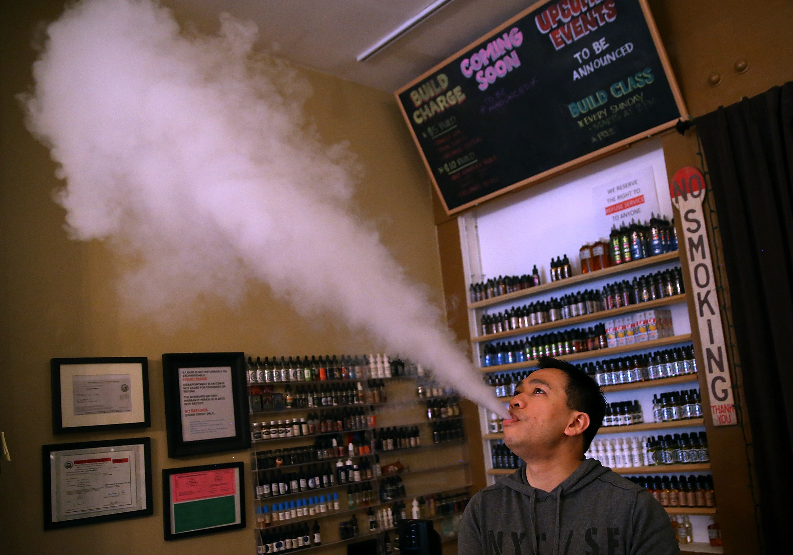A man blows e-cigarette vape smoke into the air at a smoke shop.