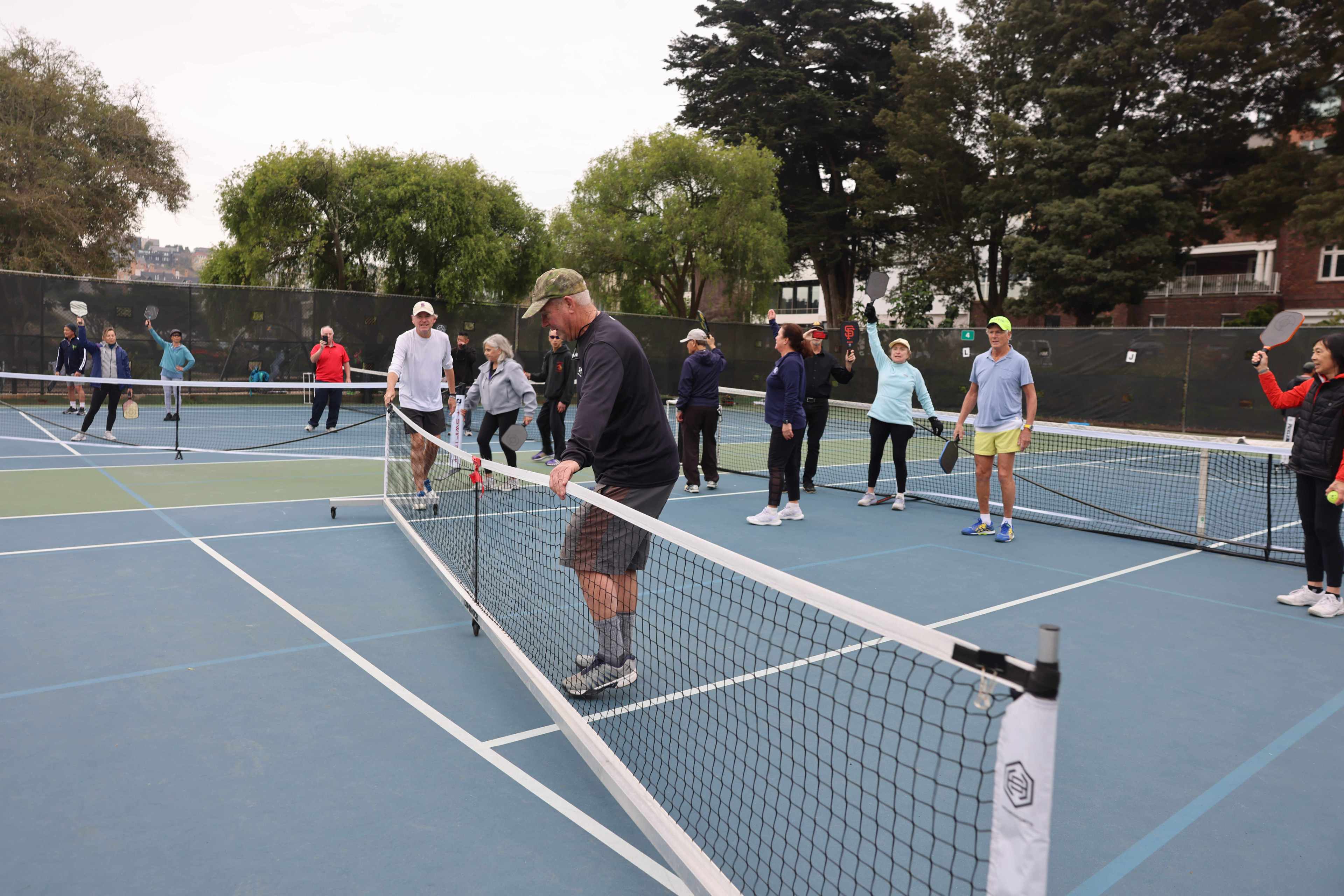 A group of people with paddles on a pickleball court remove a pickleball net.