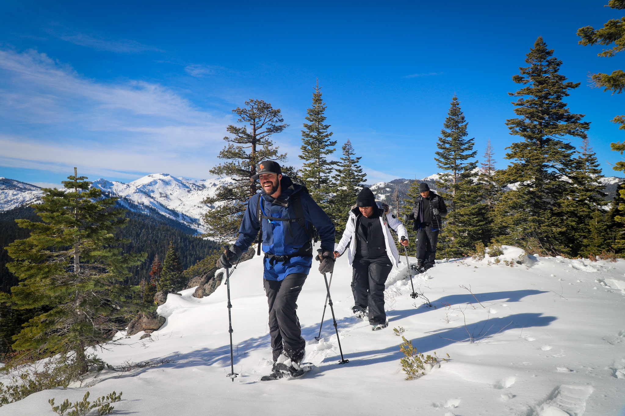 Three people snowshoe in Tahoe holding poles with the snowy Sierra mountains behind them.