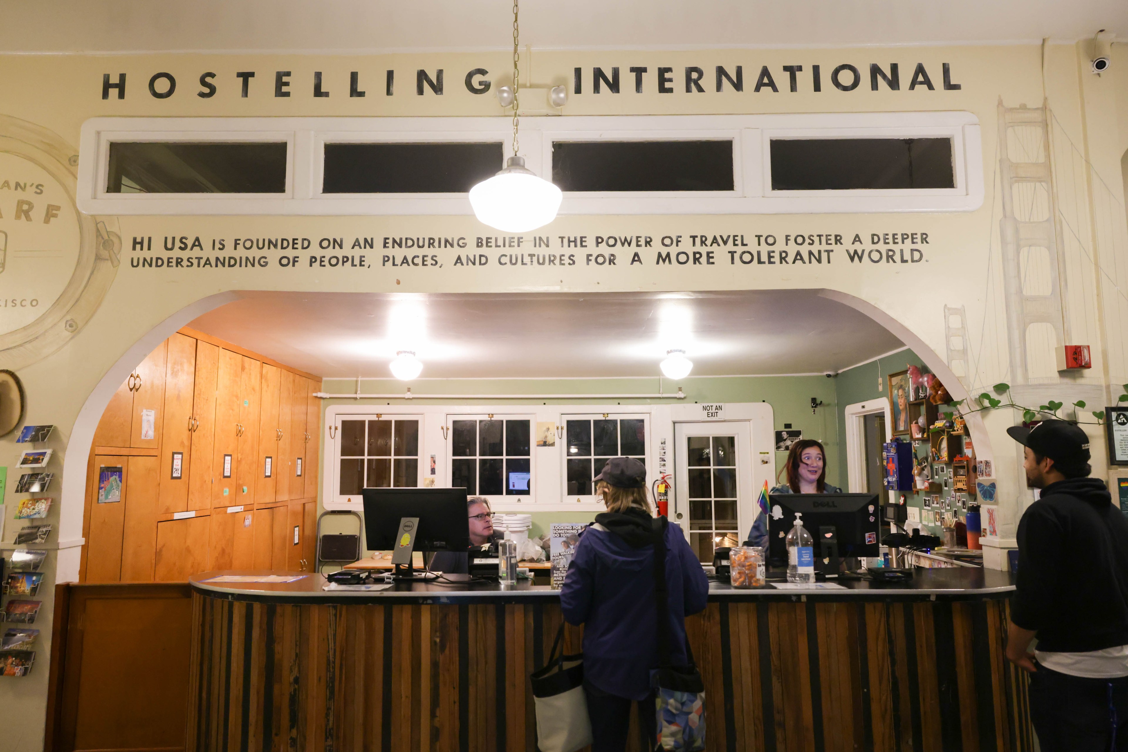 A hostel lobby with guests at the reception, wooden decor, and a mission statement for cultural understanding.