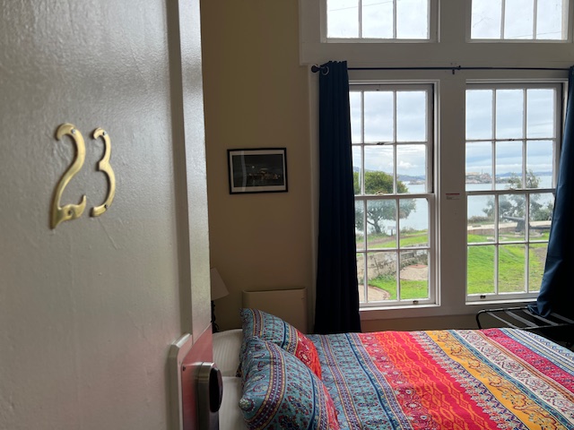 A cozy room with a colorful bedspread, a number &quot;23&quot; plaque on the wall, and a window overlooking a serene outdoor view.