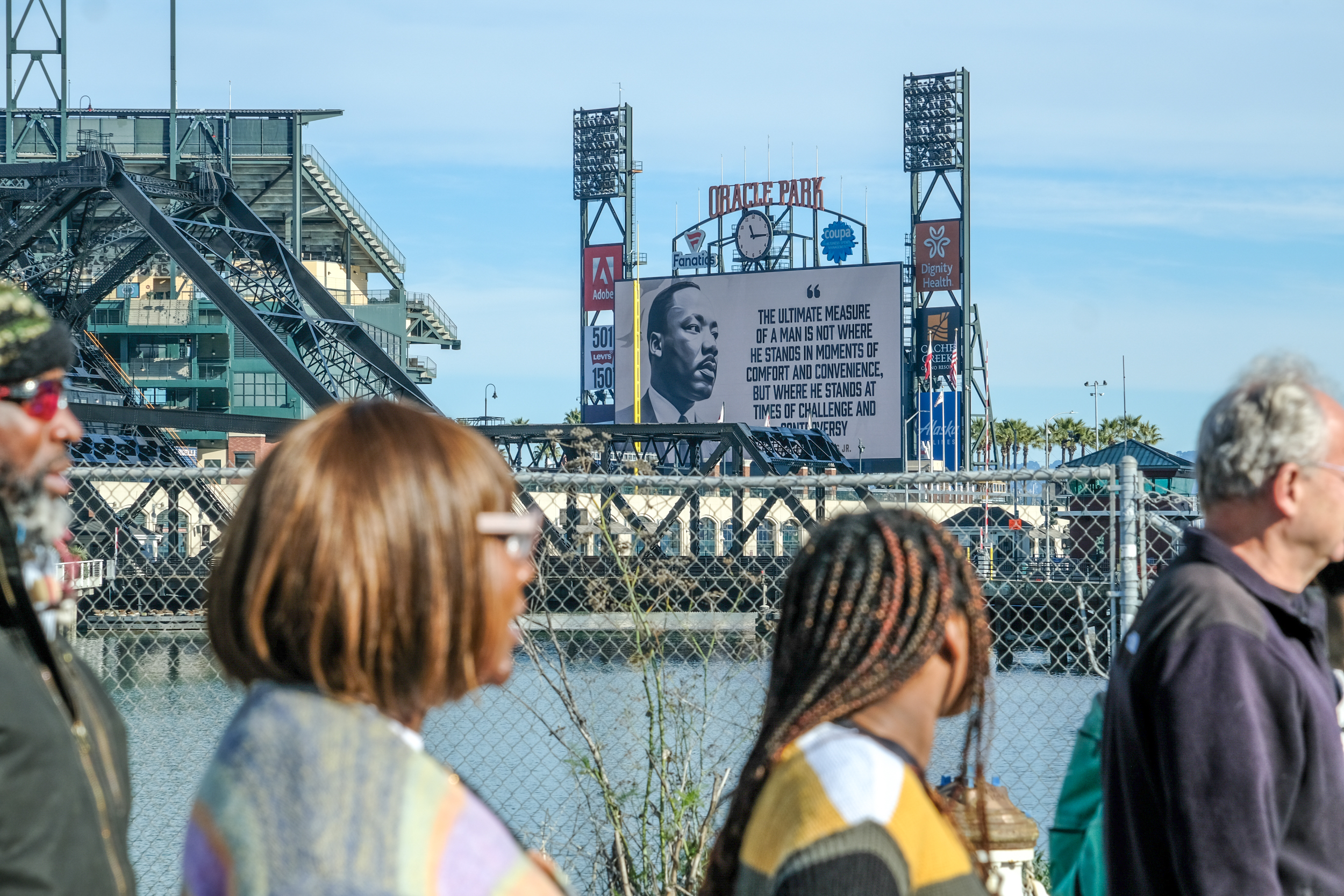 People view a ballpark with an MLK quote on the scoreboard overlooking water.