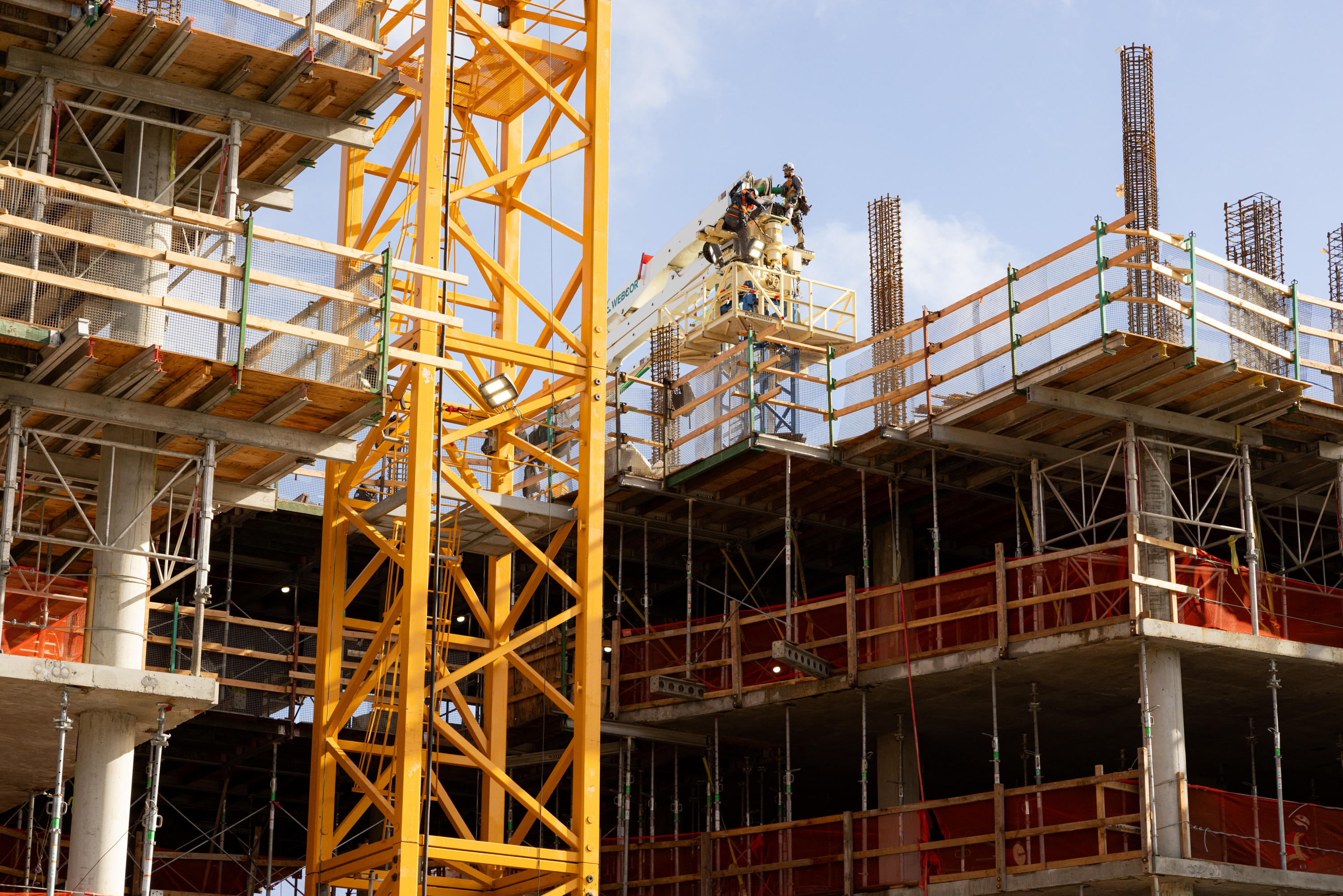 Construction site with a yellow crane, workers on scaffolding, and concrete building floors under a clear sky.
