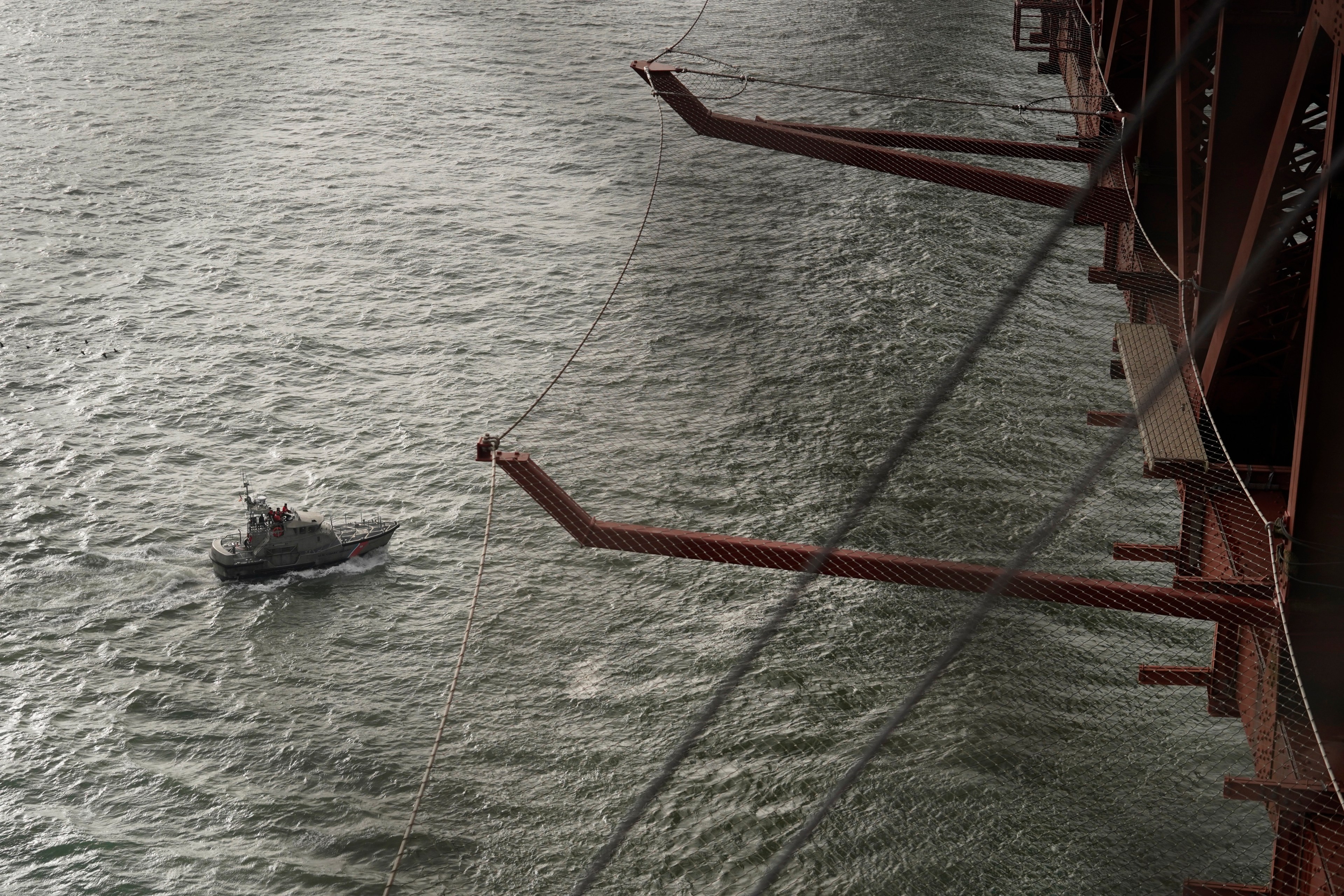 A ship passes below netting on side of red bridge