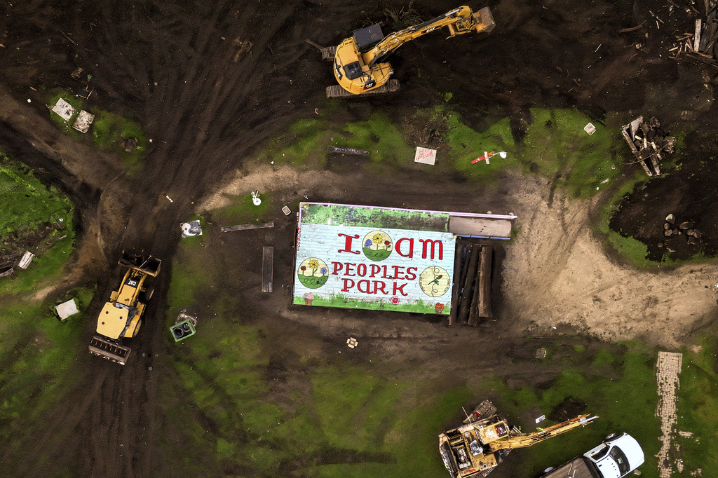 Aerial view of construction: machinery, debris around a mural reading &quot;I AM PEOPLES PARK&quot; on a rooftop.