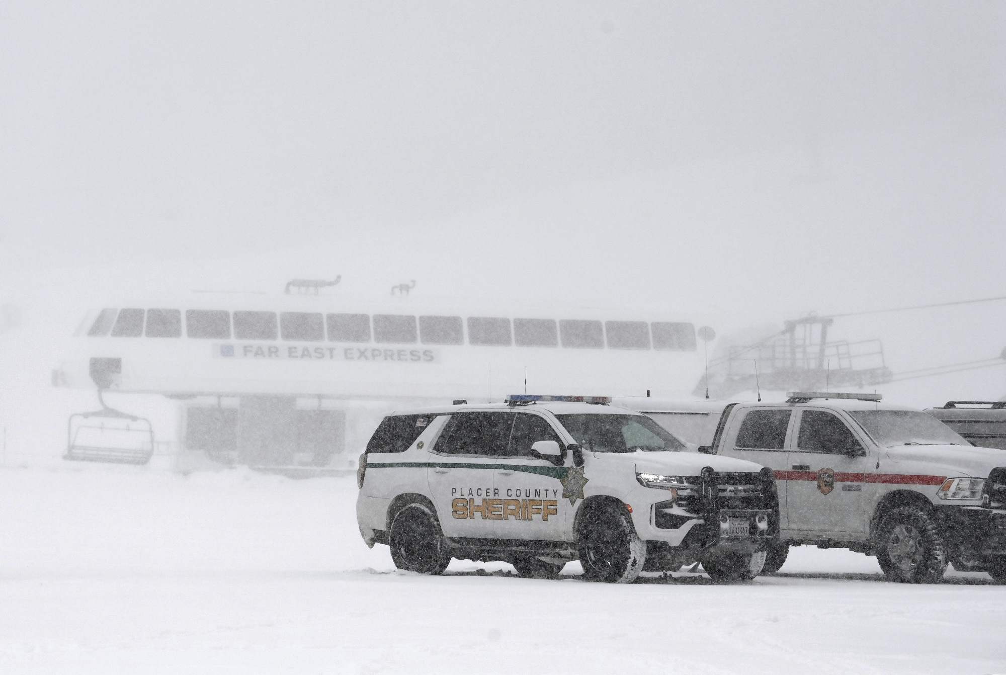 Vehicles parked with ski lift in the background as snow falls