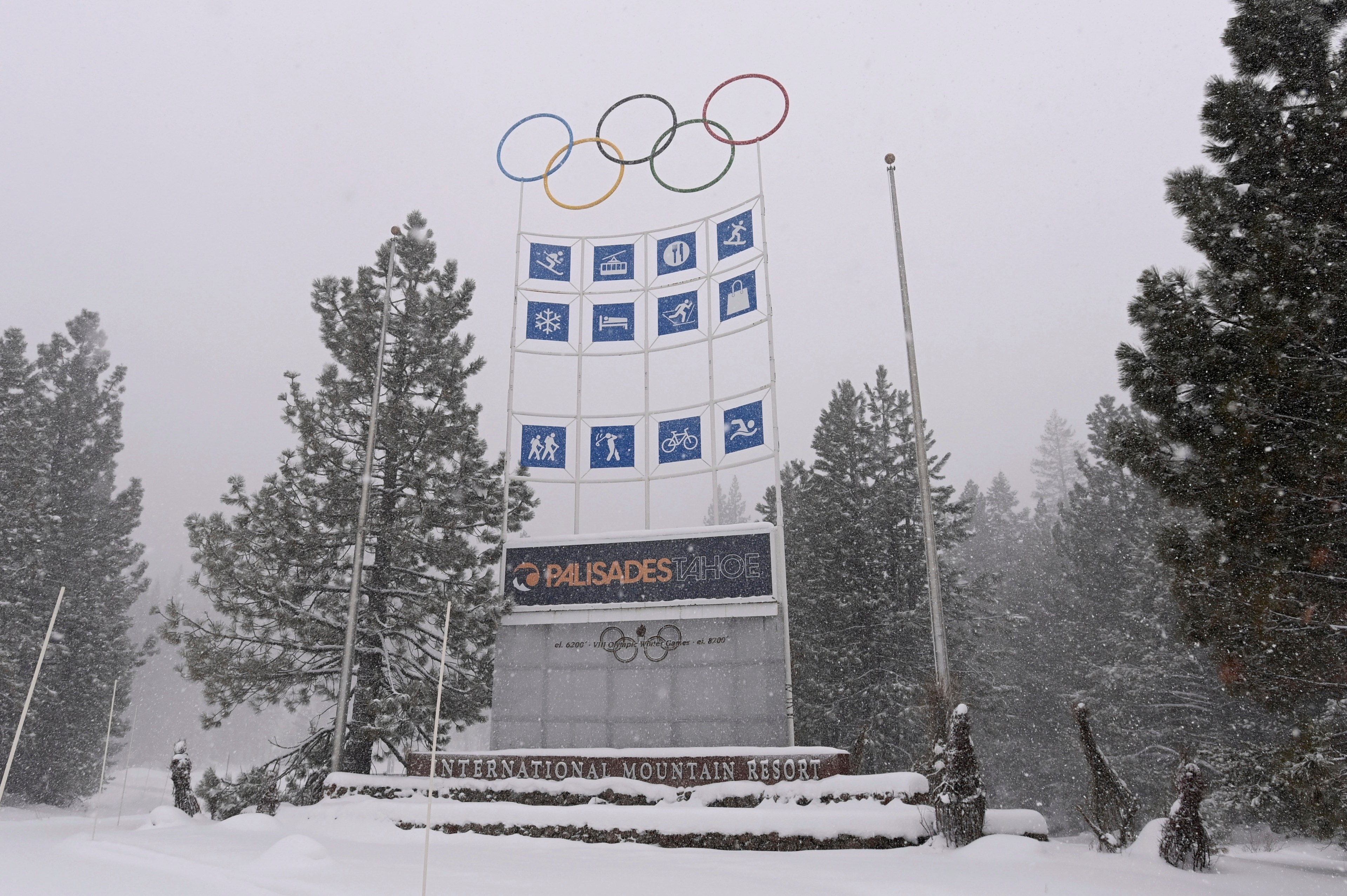 Snow falls on a ski resort entrance sign featuring olympic rings