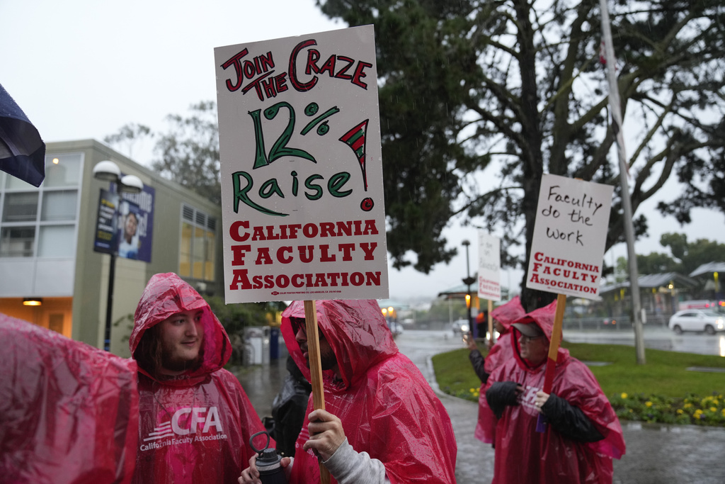 People in red raincoats protest under the rain, holding signs for a 21% raise by the California Faculty Association.