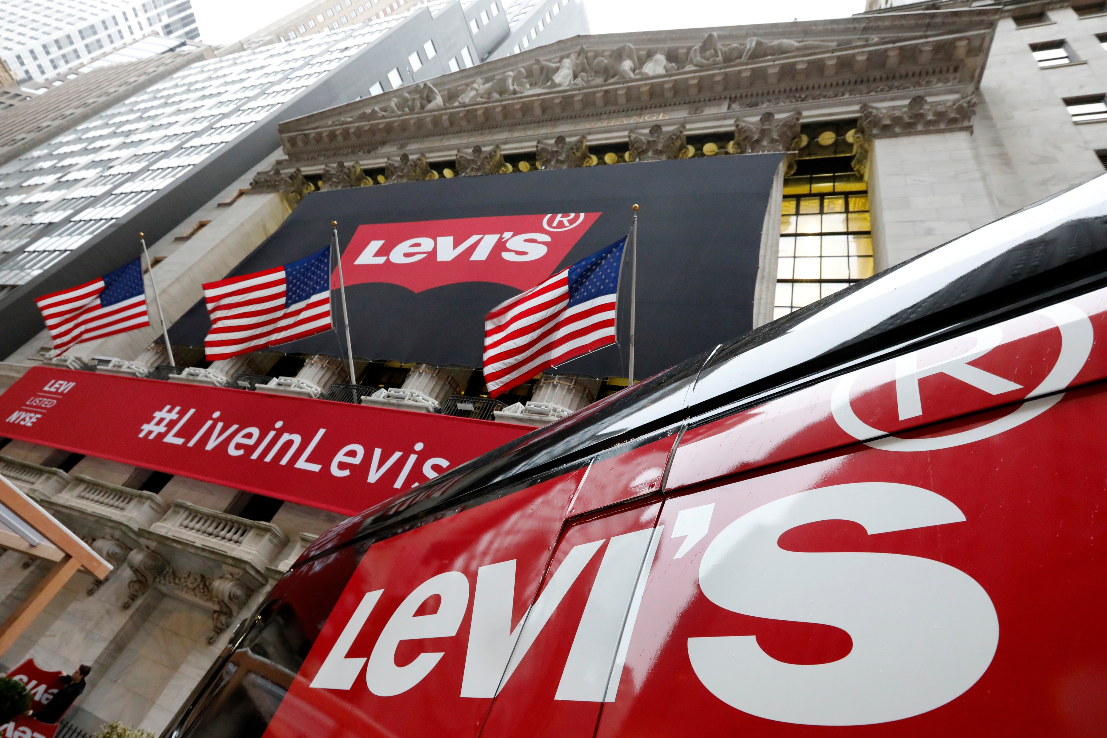The photo shows a Levi's branded banner, American flags, and a red vehicle with Levi's logos in an outdoor urban setting.