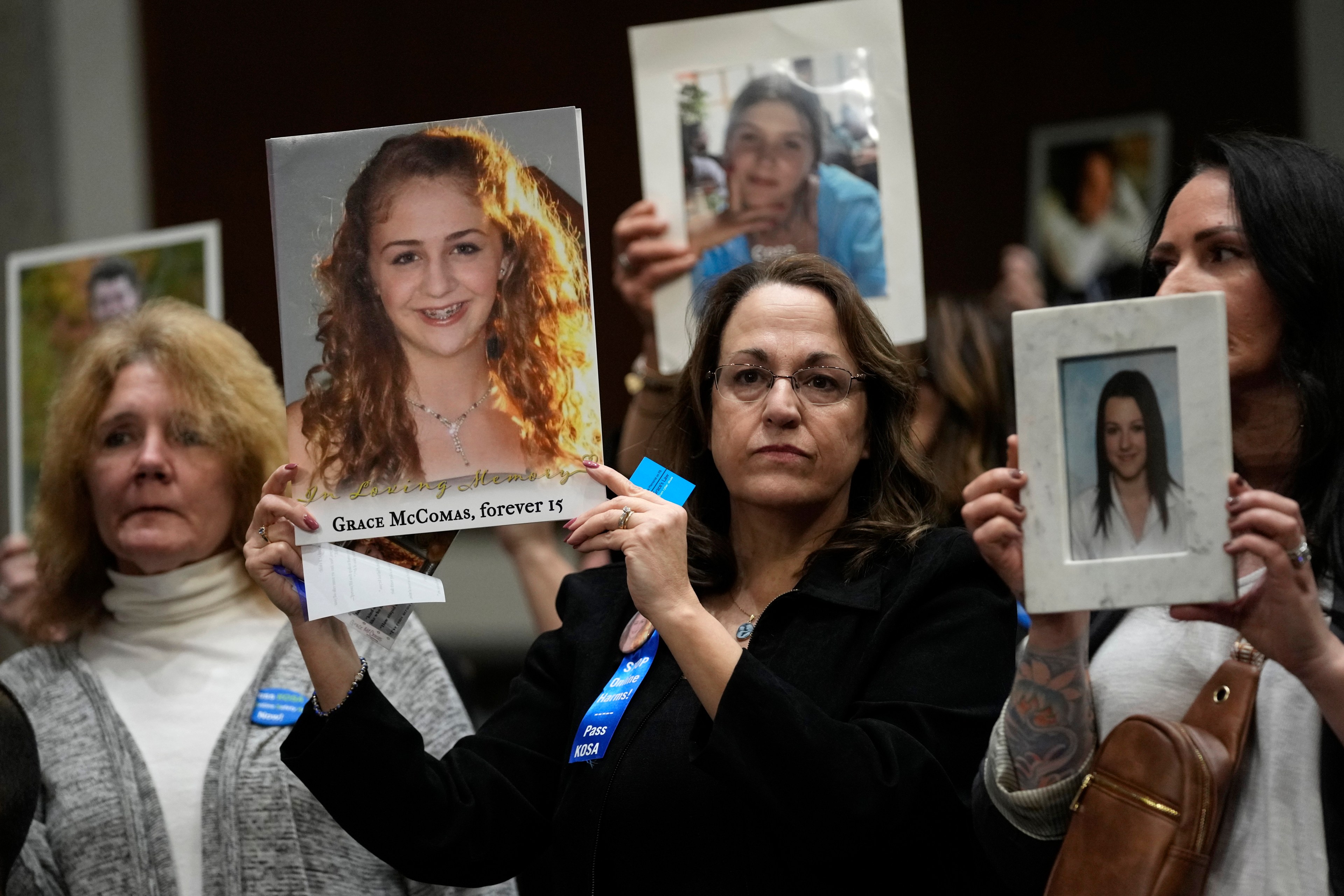 Women wearing blue ribbons hold up pictures of young people