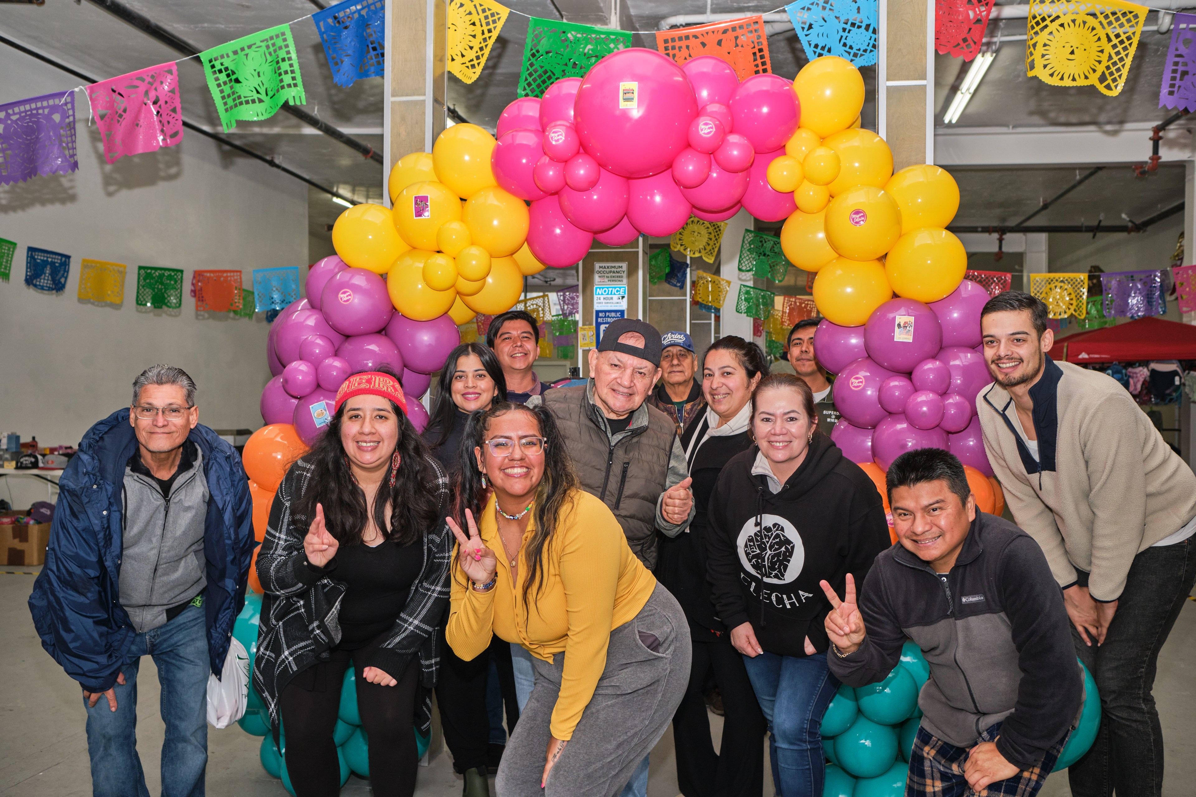 A group of smiling people posing at a festive gathering with colorful balloons and decorative paper in the background.