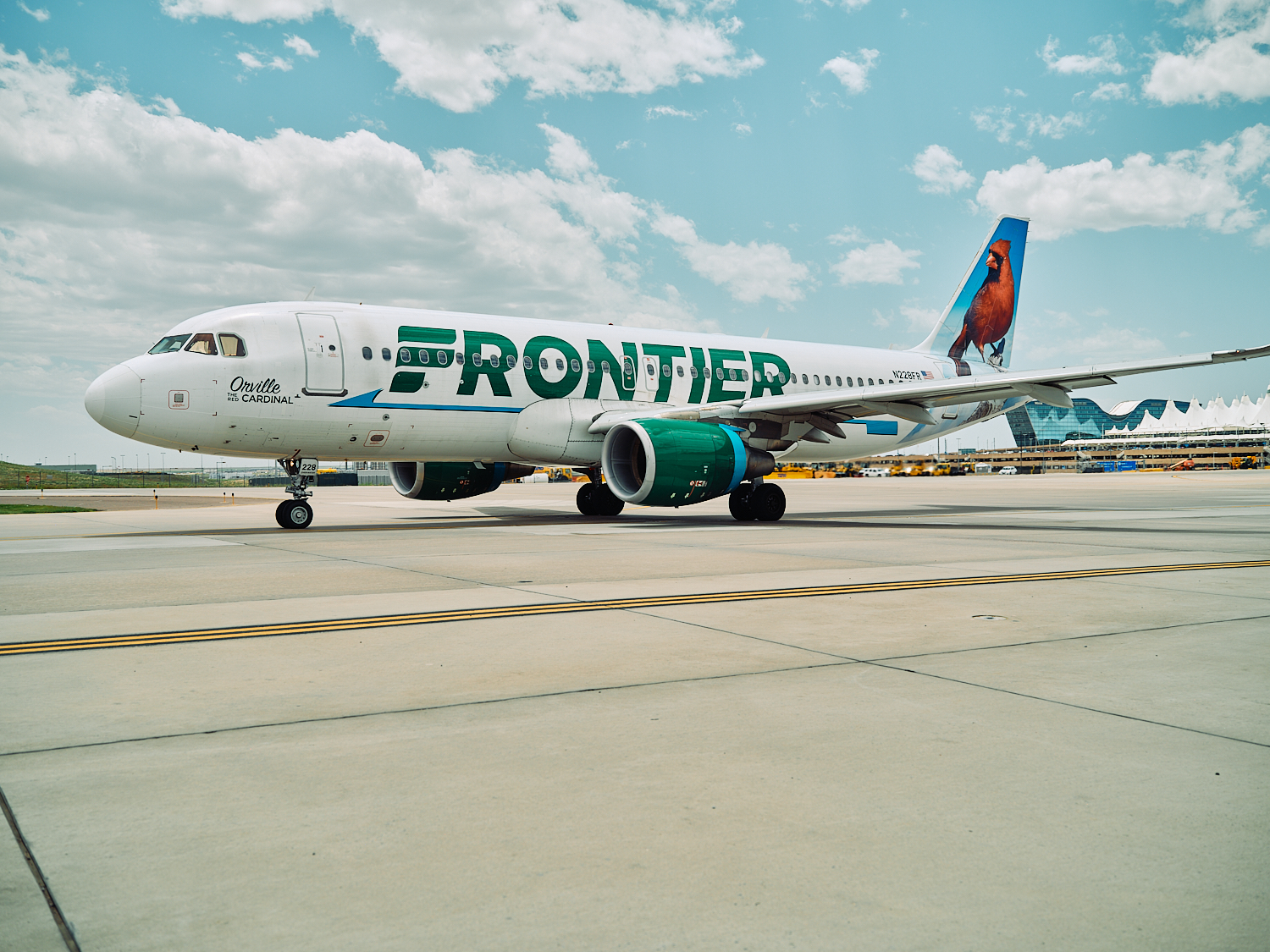 A Frontier Airlines plane with a cardinal on the tail taxis on the tarmac under a cloudy sky.