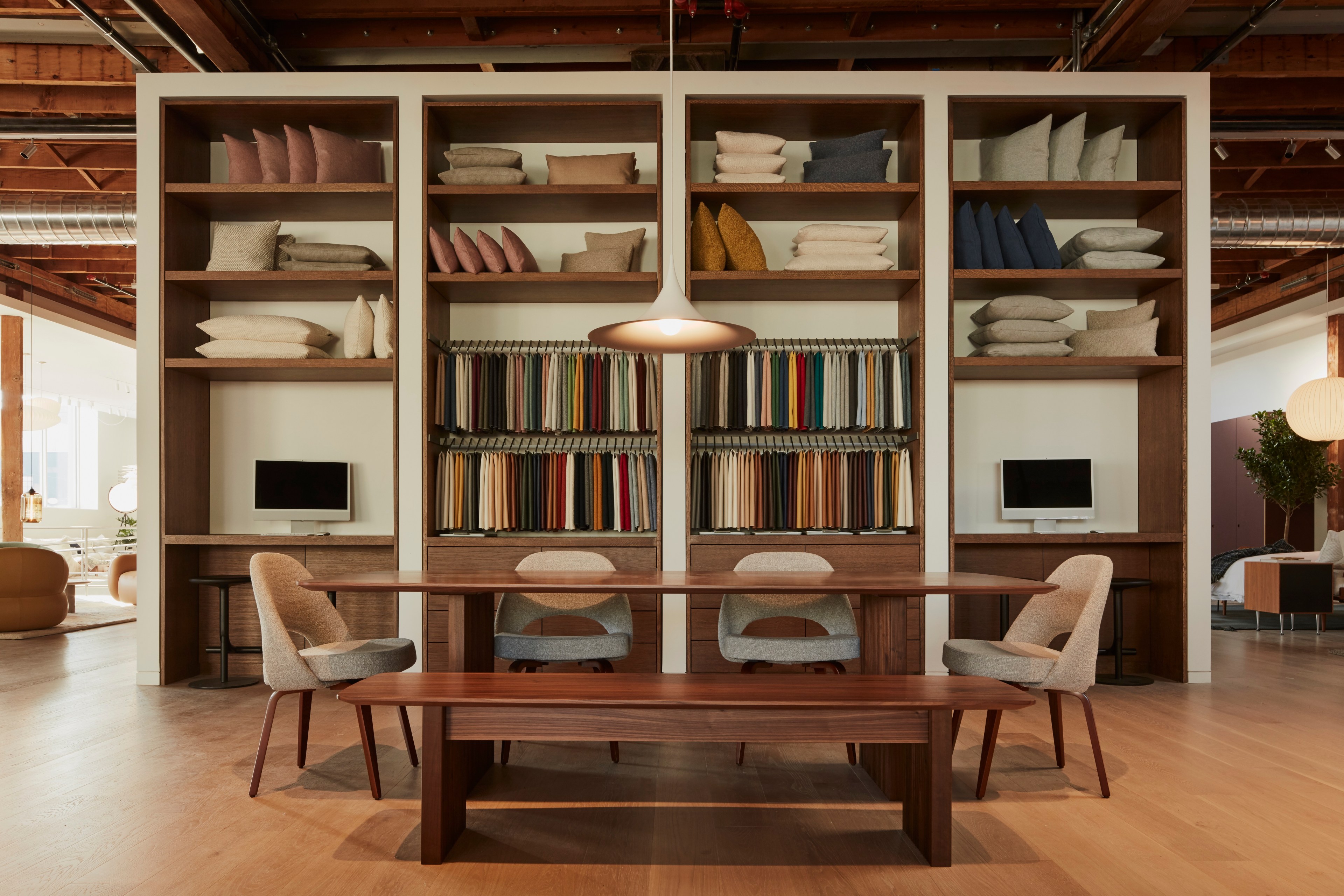 Floor-to-ceiling shelves hold textile samples behind a wooden dining room table and modern chairs.
