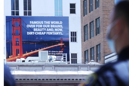 A billboard with the Golden Gate Bridge, a critical message about fentanyl, foregrounded by a blurry officer's profile.