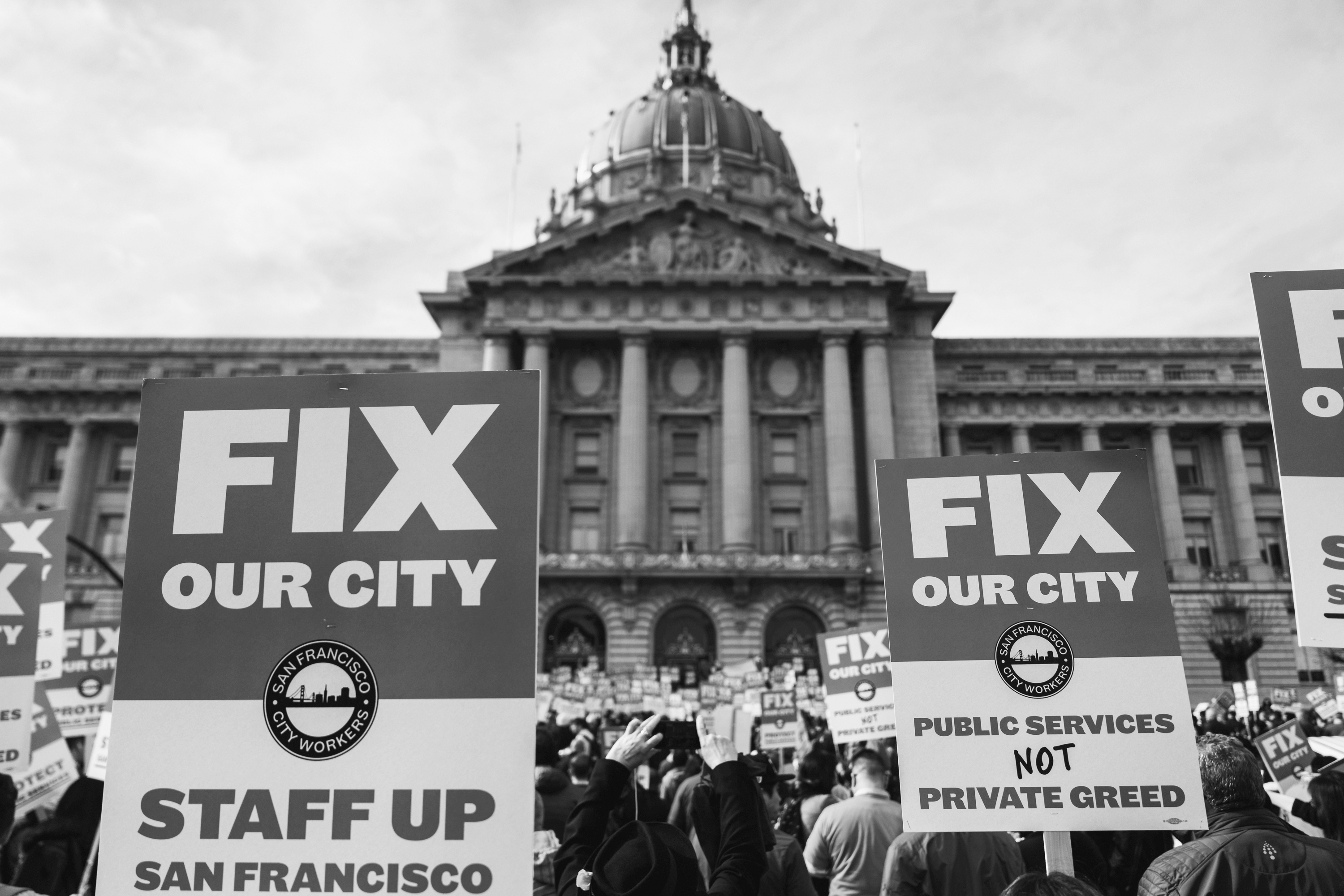 Protesters hold signs saying "FIX OUR CITY" in front of San Francisco's City Hall.