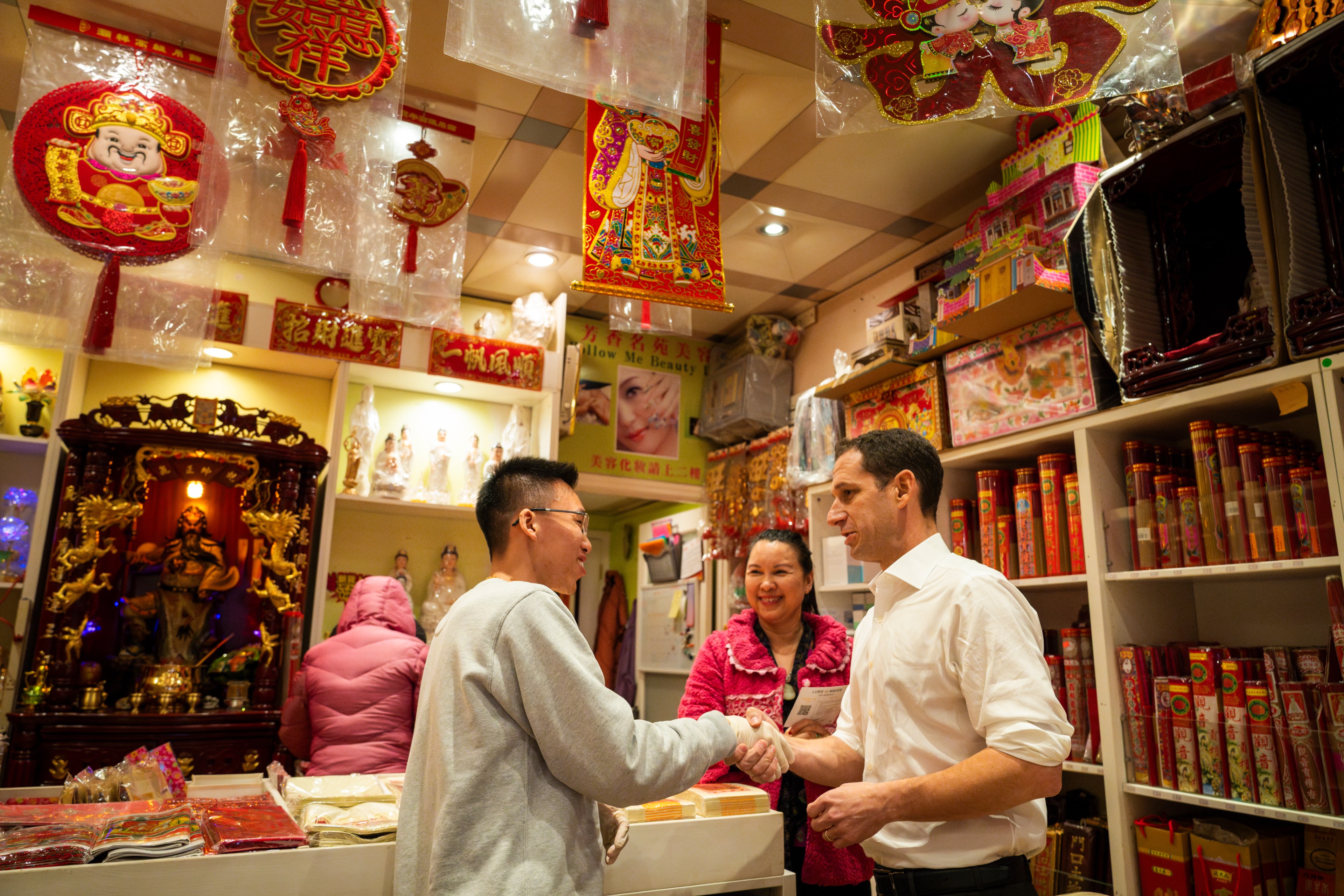 A vibrant shop with people, Chinese decorations, and altar. Two individuals engage in a handshake.
