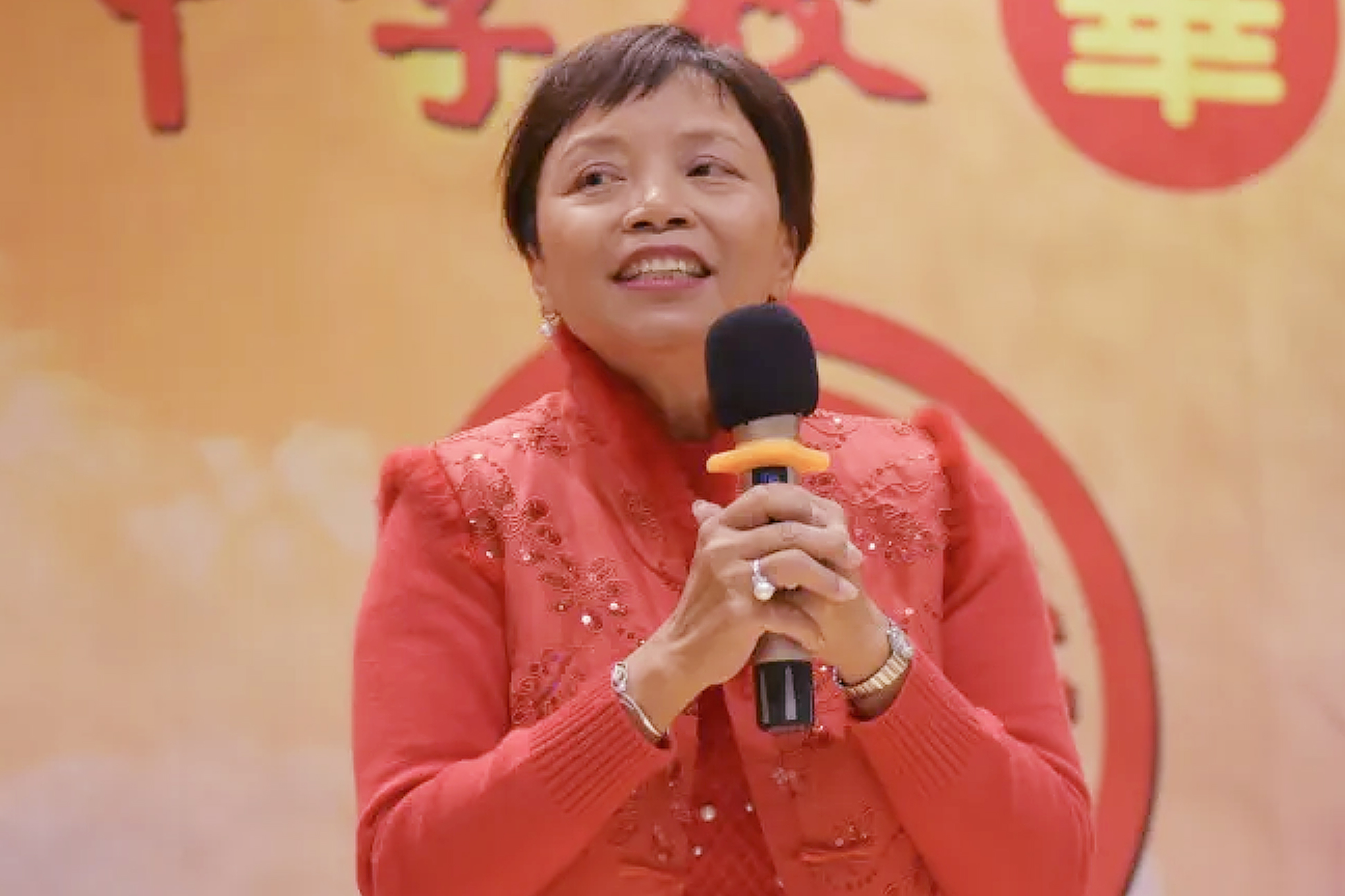 A woman in a red shirt holds a microphone.