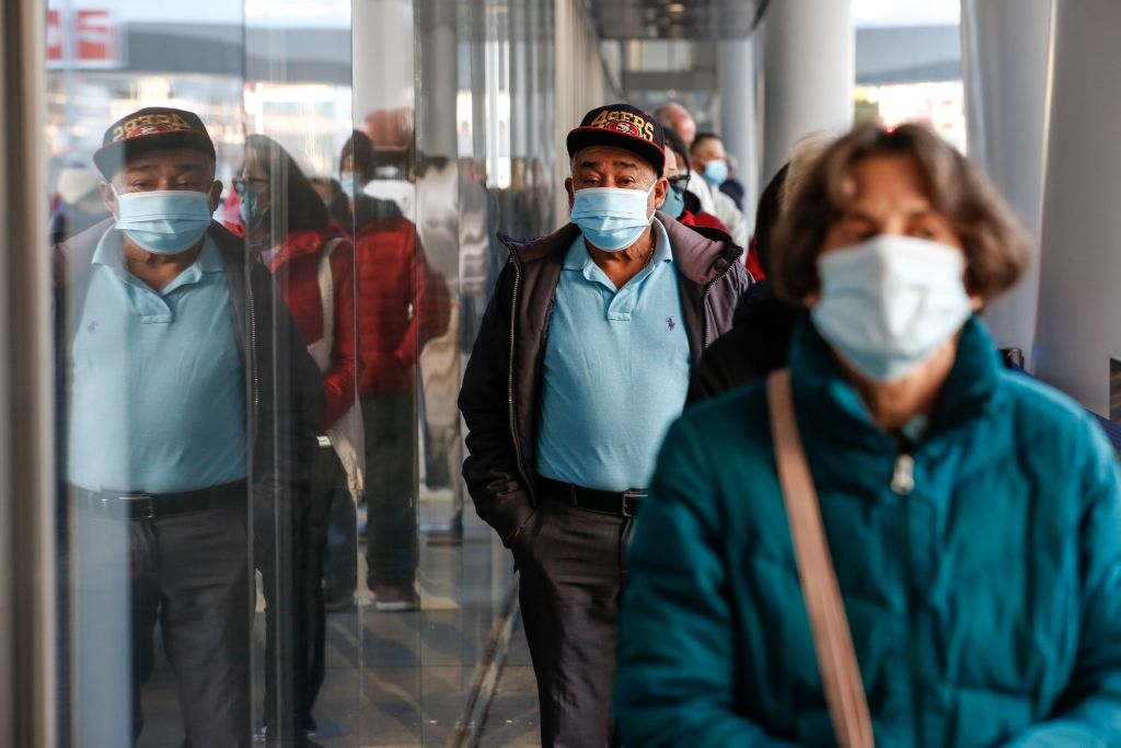 People stand in a line while wearing surgical masks.