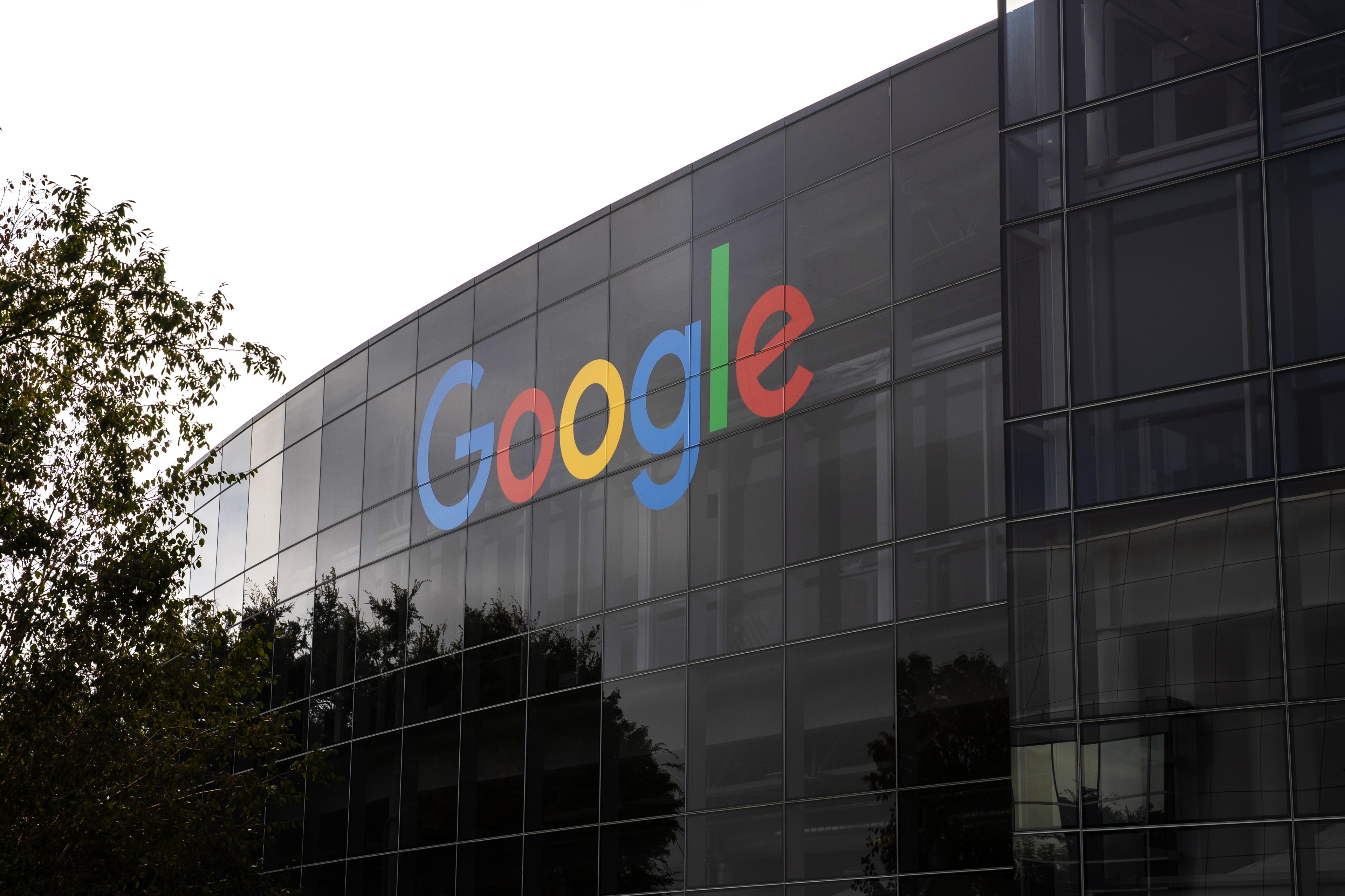 A Google logo in colorful letters on a glass-walled building, with trees nearby.