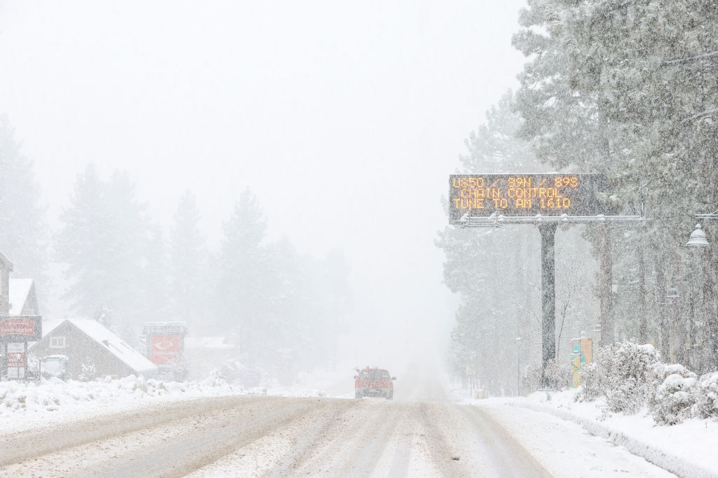 A blizzard obstructs the view of a mountain highway.
